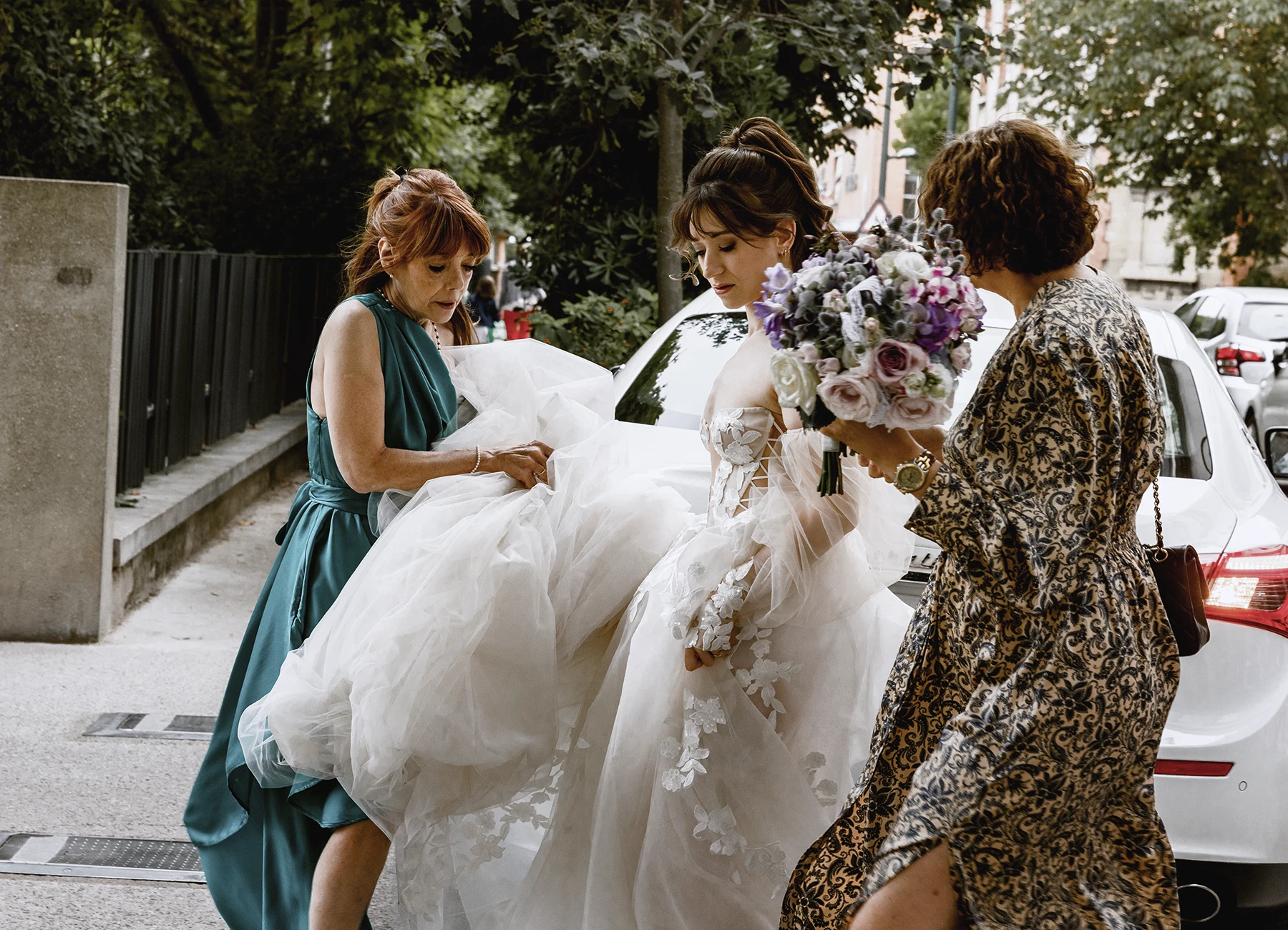 Mère de la mariée et une amie tenant la traîne pendant qu'elle monte les marches. Photo par Laurène Zabary.
