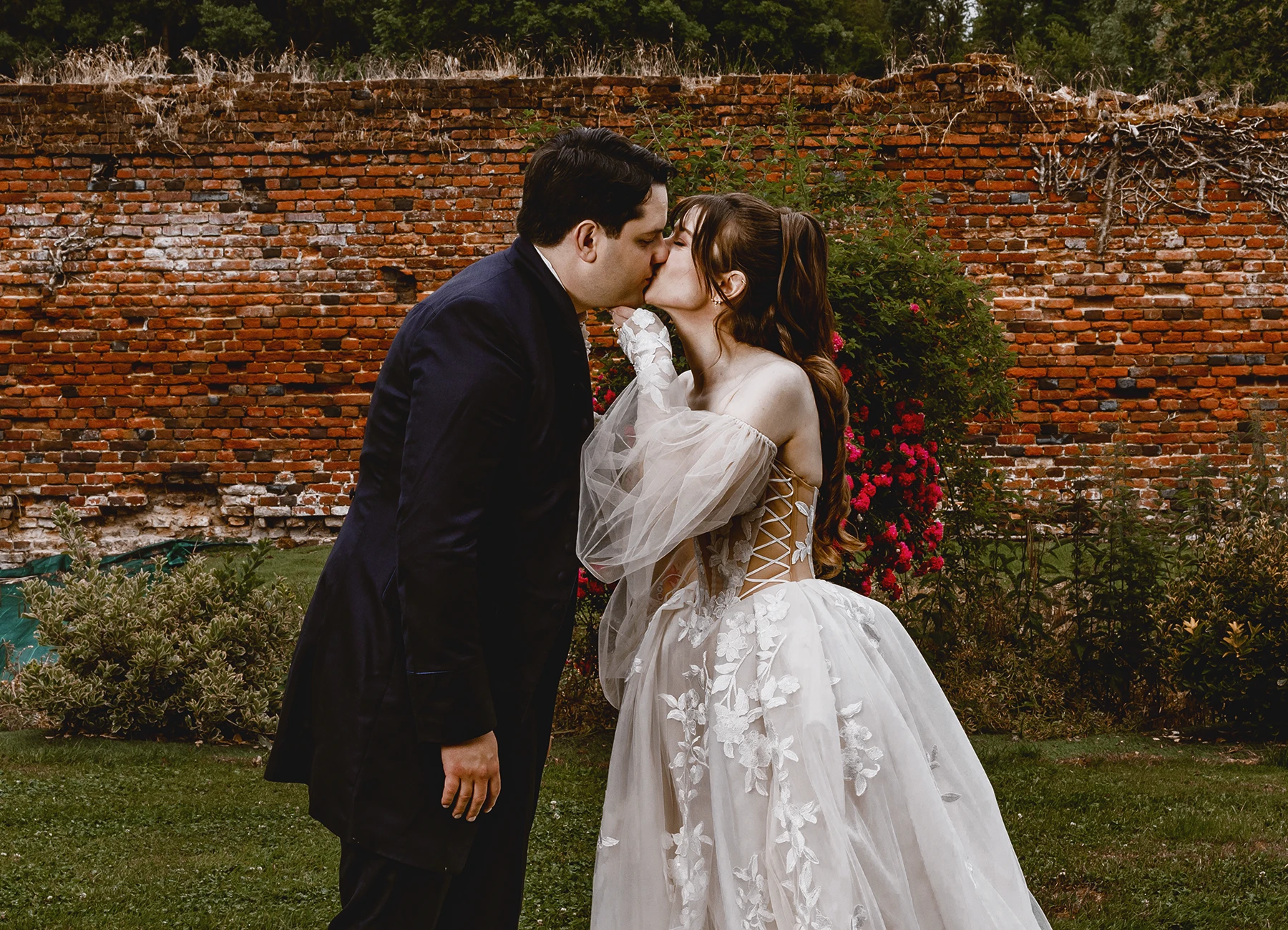 Mariés s'embrassant devant un mur de briques lors d'un shooting de groupe en extérieur à Quesmy, photo par Laurène Zabary