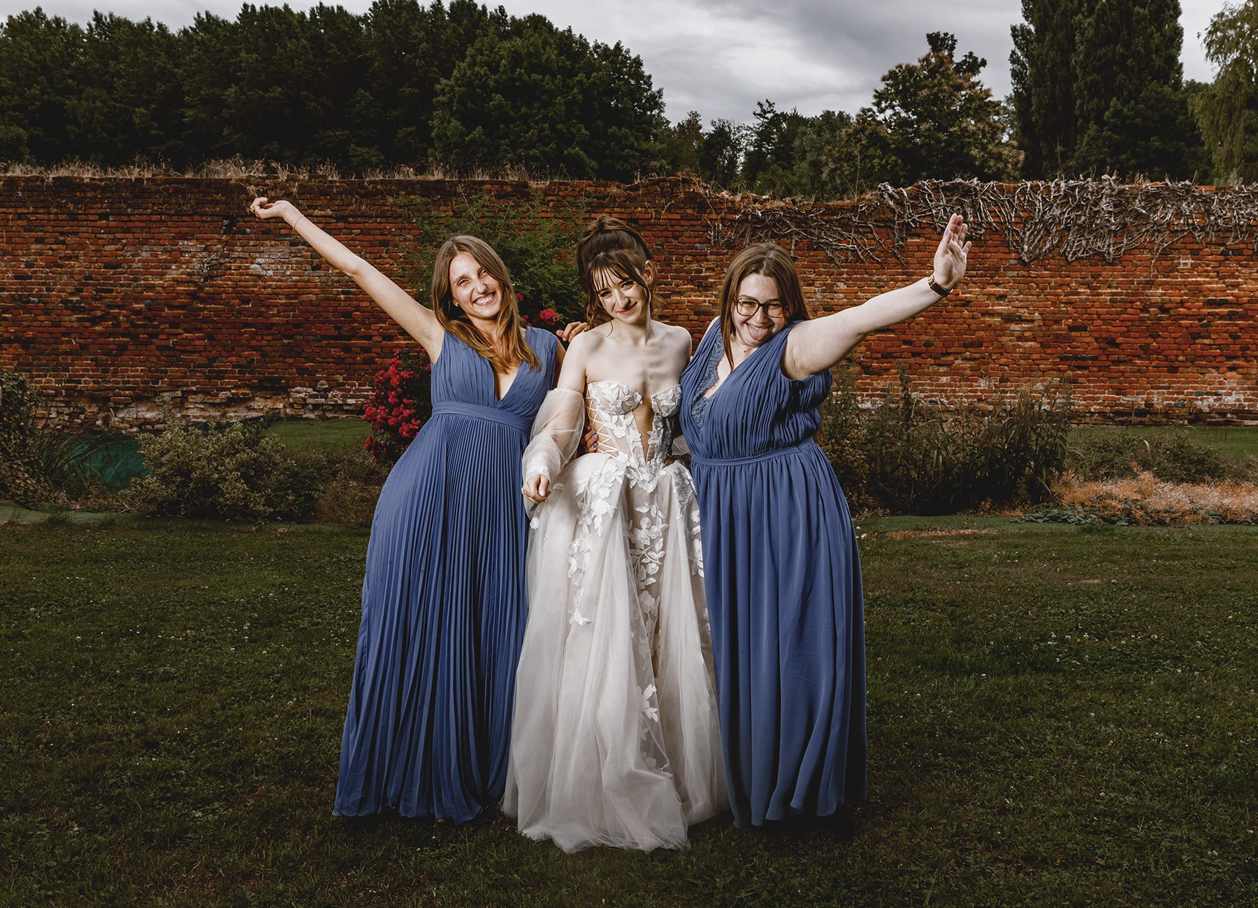 Mariée avec ses demoiselles d'honneur en robes bleues, bras levés en riant à Quesmy, photo par Laurène Zabary