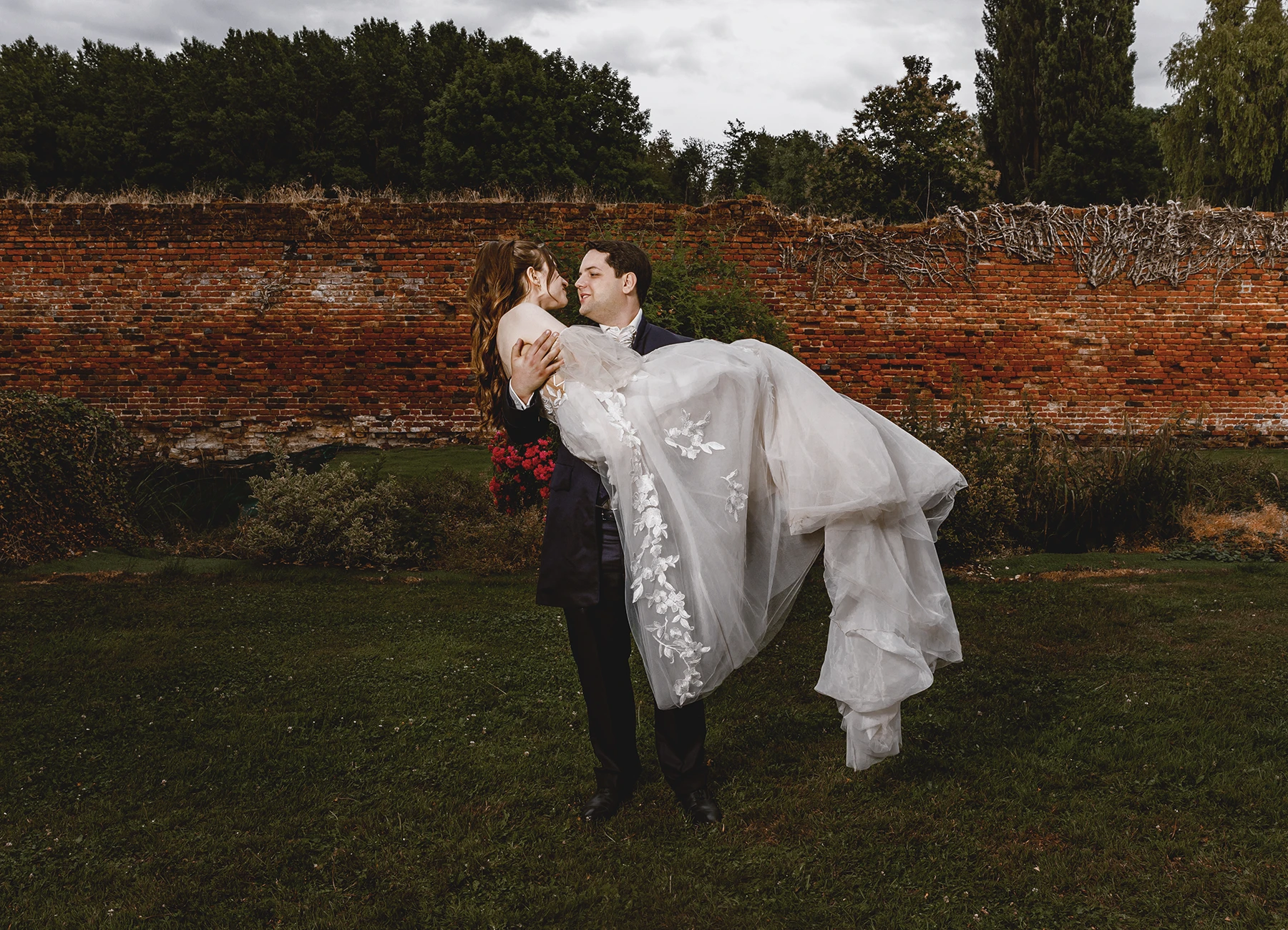 Marié portant la mariée dans ses bras devant un mur de briques à Quesmy, photo de mariage par Laurène Zabary