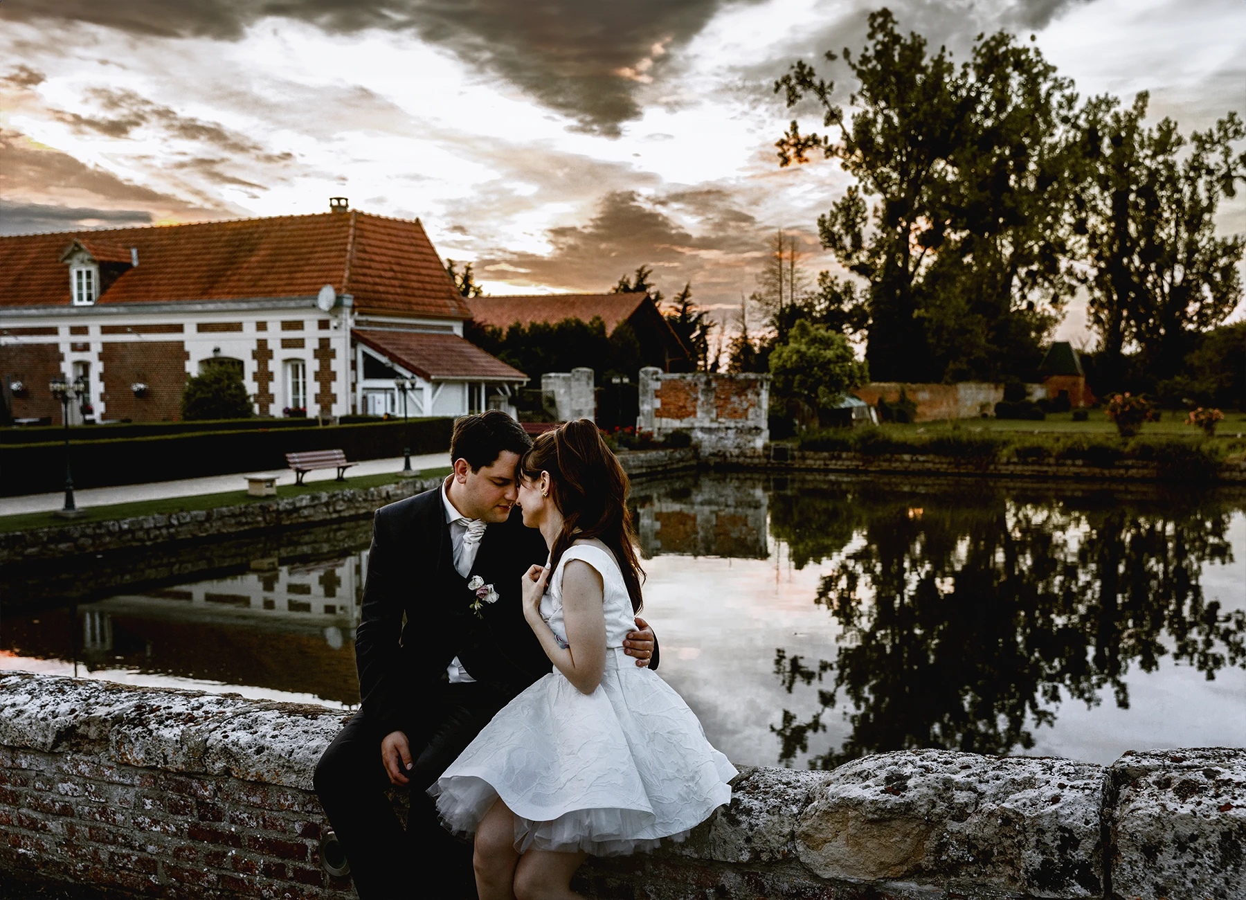 Mariés assis sur une margelle de pont au château de Quesmy, golden hour, reflet dans l'étang, photo par Laurène Zabary