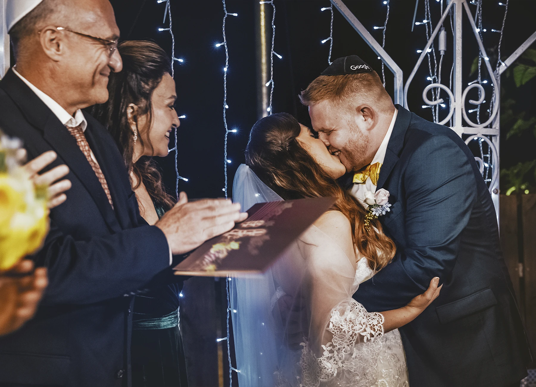 Mariés s'embrassant sous la houppa avec les parents applaudissant à Jaffa - Laurène Zabary