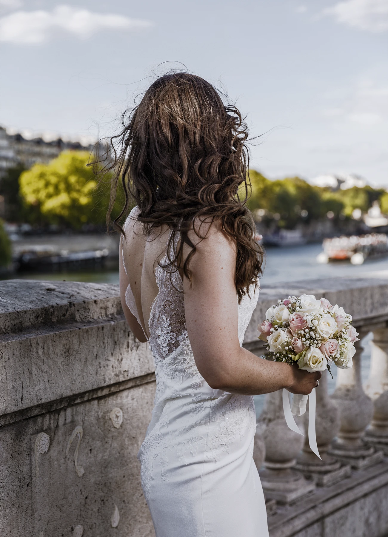 Mariée de dos tenant un bouquet de fleurs avec la Seine en arrière-plan sur le pont Bir Hakeim à Paris, capturée par Laurène Zabary.