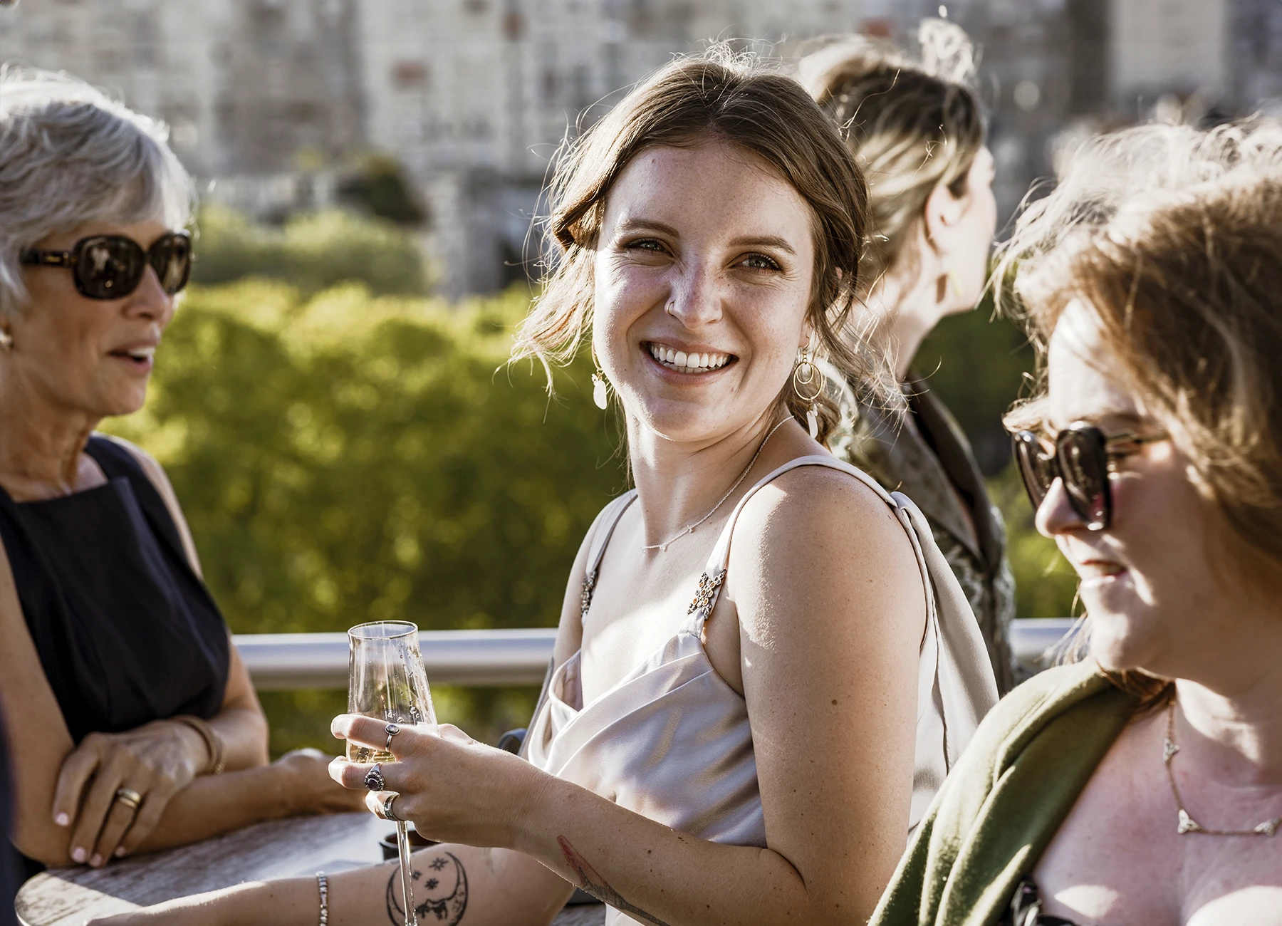 Jeune femme en robe grise tenant une flûte de champagne au vin d'honneur du mariage au Rooftop Grenelle à Paris, photographiée par Laurène Zabary.