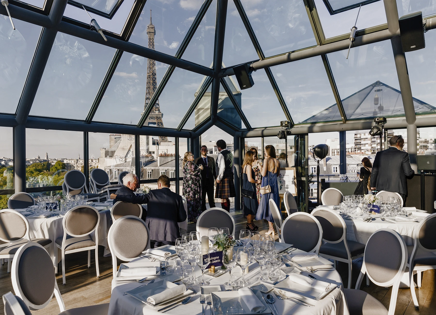 Salle principale du Rooftop Grenelle avec vue sur la tour Eiffel à travers la verrière, lors d'un mariage à Paris, capturée par Laurène Zabary.
