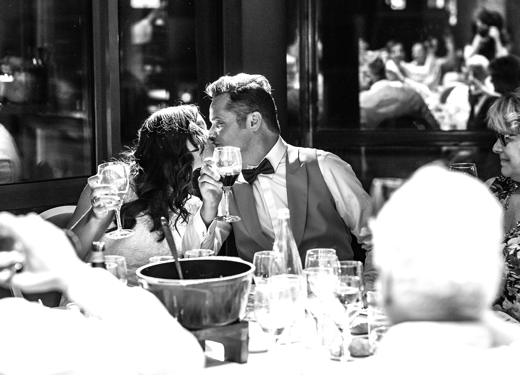 Les mariés s'embrassant assis à leur table lors du repas de mariage au Rooftop Grenelle à Paris, en noir et blanc, capturés par Laurène Zabary.