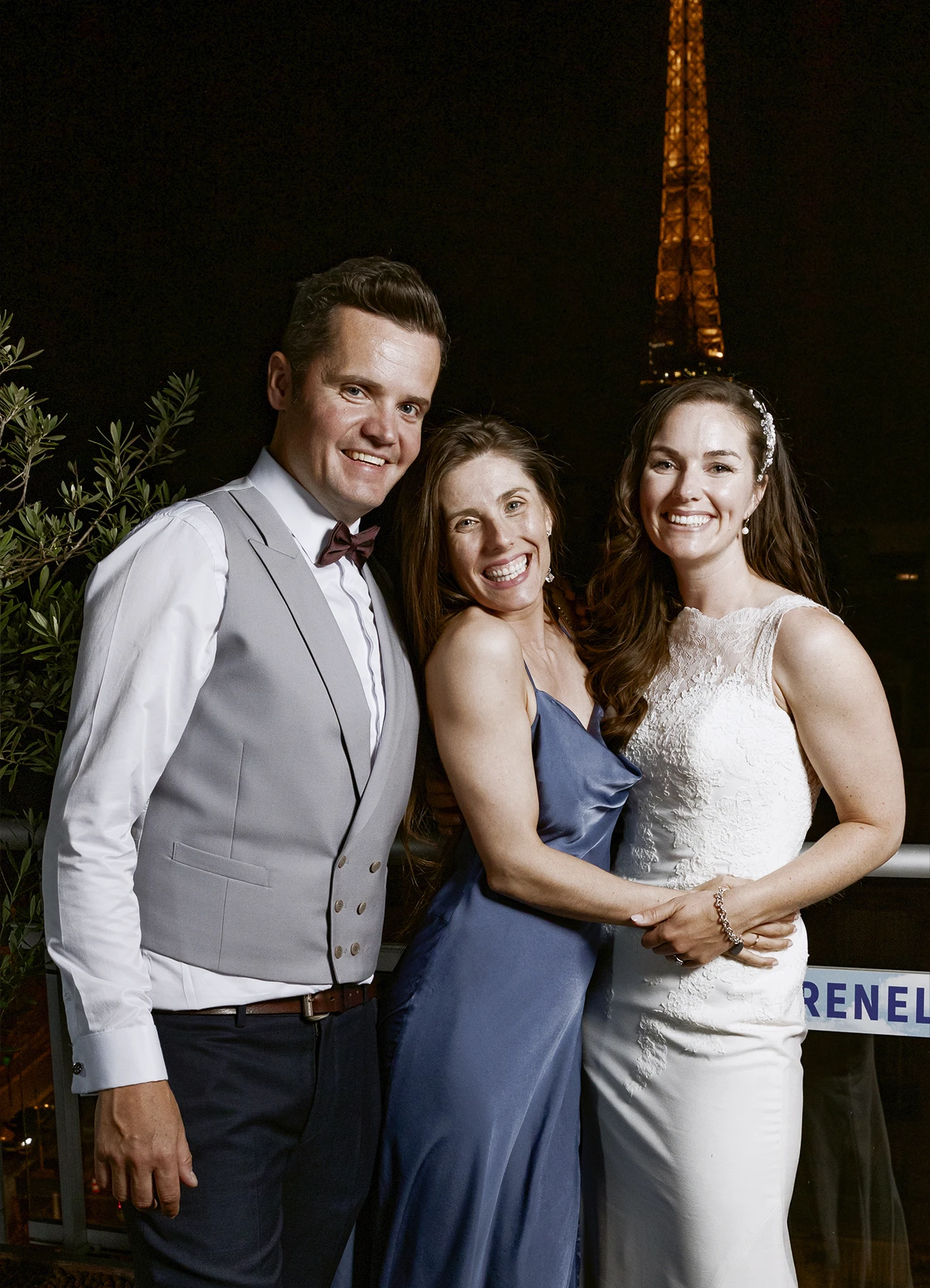 Mariés posant avec une invitée sur le rooftop avec la tour Eiffel illuminée en arrière-plan, capturés par Laurène Zabary, photographe de mariage à Paris