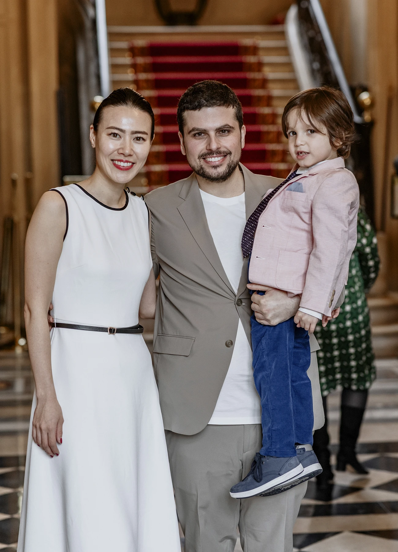 Le marié en costume marron tenant un petit garçon en costume dans ses bras. Les trois sourient à la caméra