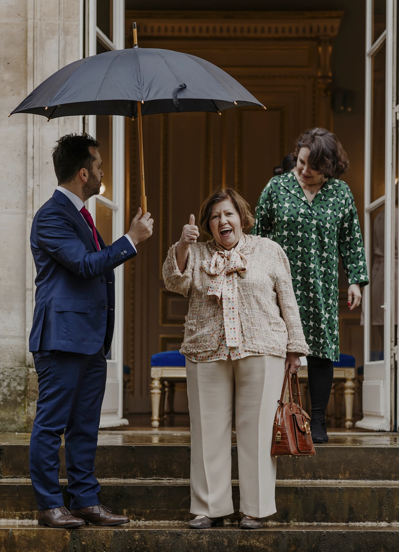 La grand-mère, sous un parapluie, descend les escaliers de la mairie du 7e arrondissement de Paris.