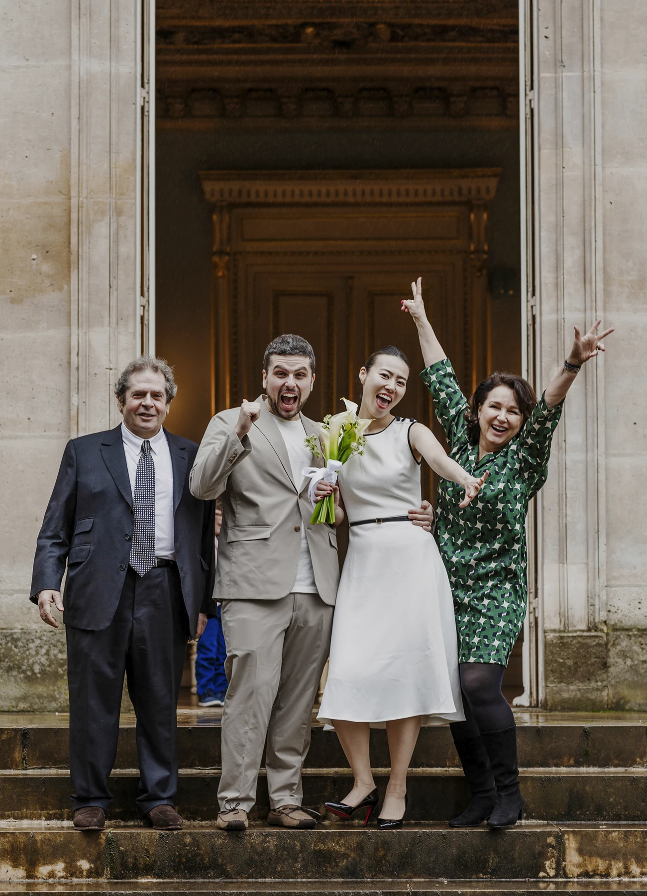 Photo de groupe des mariés avec les parents du marié sur les marches de la mairie du 7e arrondissement de Paris