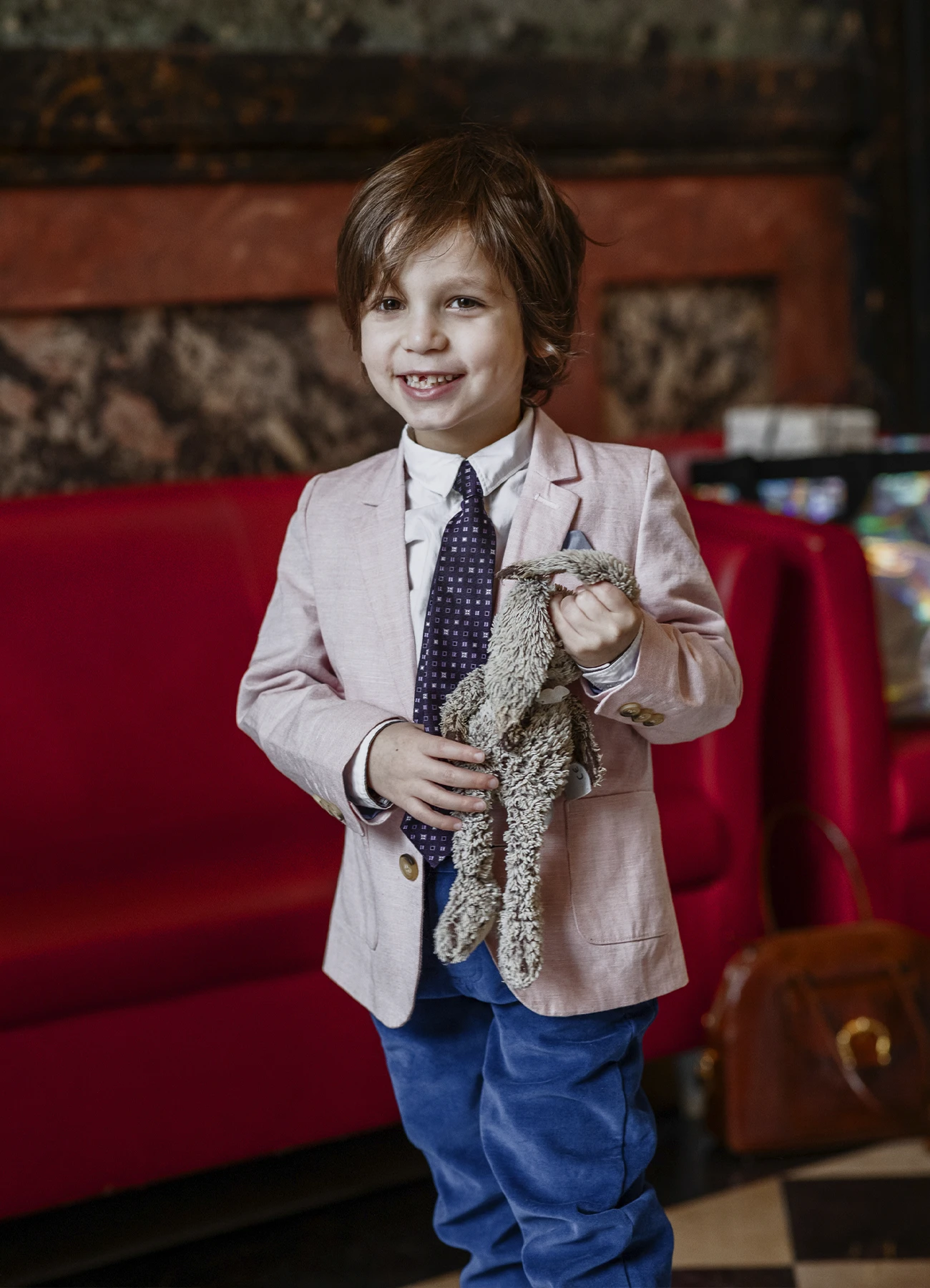Portrait d'un jeune garçon en costume bleu et rose clair, souriant à la caméra lors d'un mariage à la mairie du 7e arrondissement
