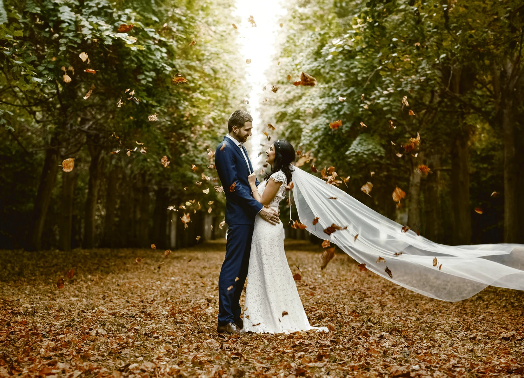 Couple de mariés en automne dans le parc du Château de Versailles, entourés de feuilles tombantes. Photo par Laurène Zabary