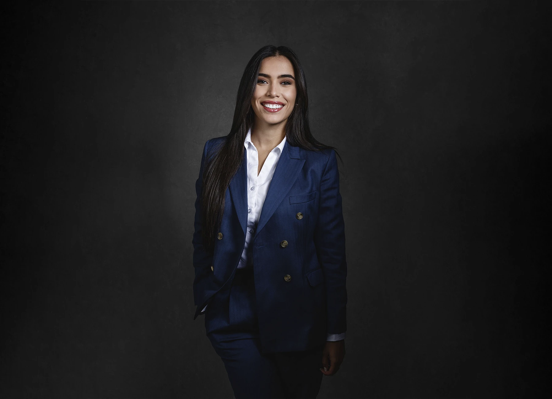 Portrait corporate en studio : femme brune en costume bleu sur fond gris foncé. Photo par Laurène Zabary.