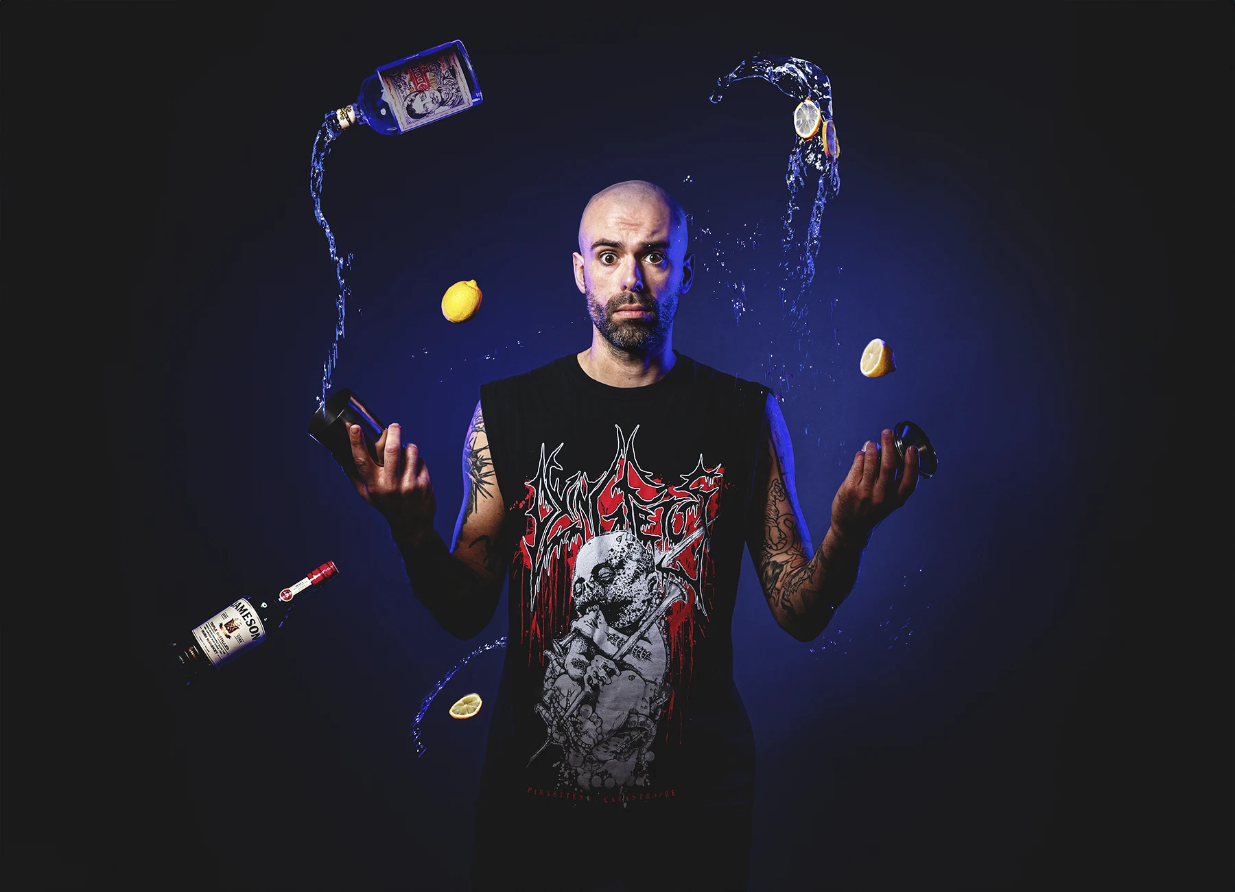 Portrait d'un barman en studio sous lumières colorées, jonglant avec des bouteilles et accessoires de cocktail. Photo par Laurène Zabary