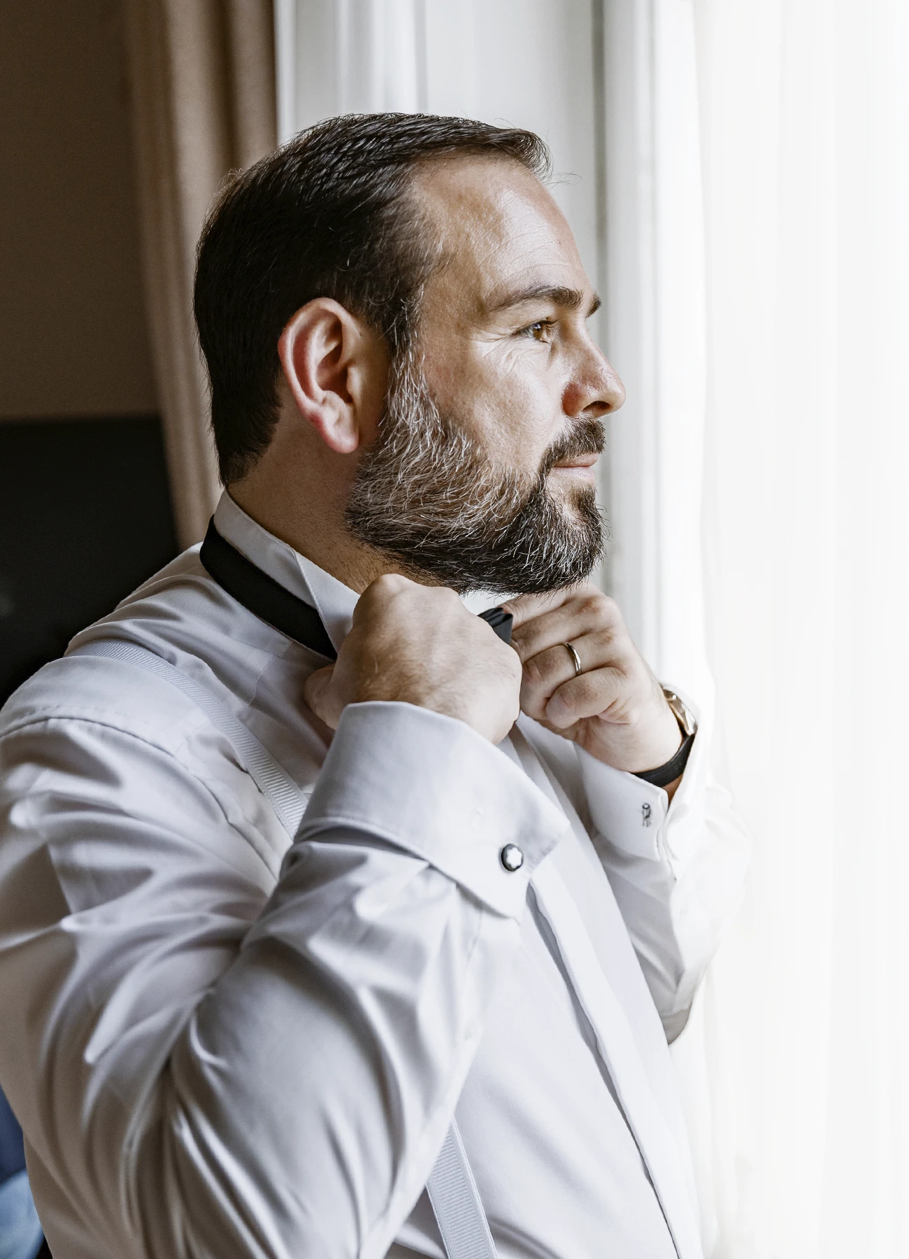 Le marié, de profil face à la fenêtre, réajustant son nœud papillon. Photo par Laurène Zabary