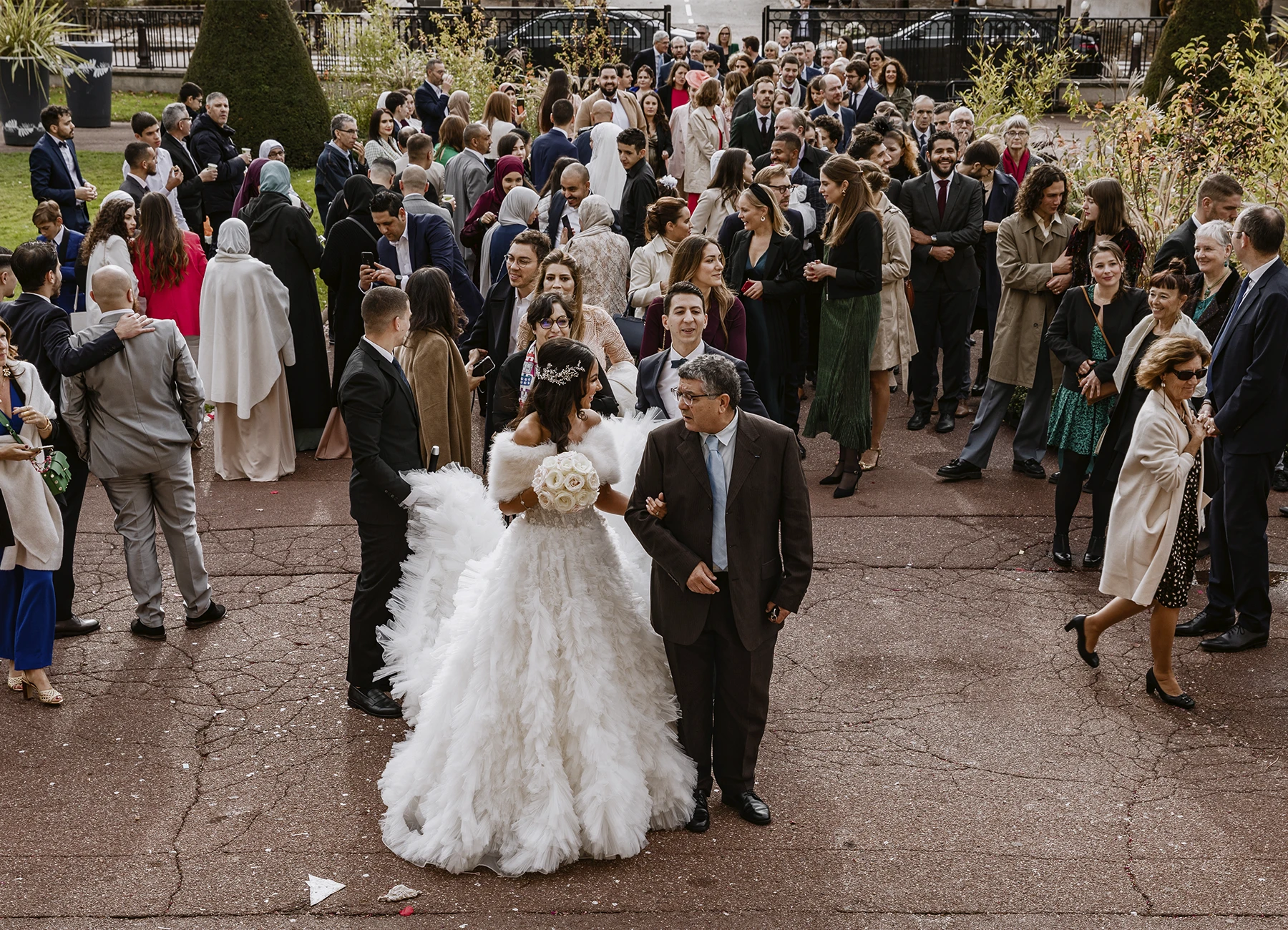 Mariée en robe blanche au bras de son père à l'entrée de la mairie, souriant à l'objectif. Photo par Laurène Zabary