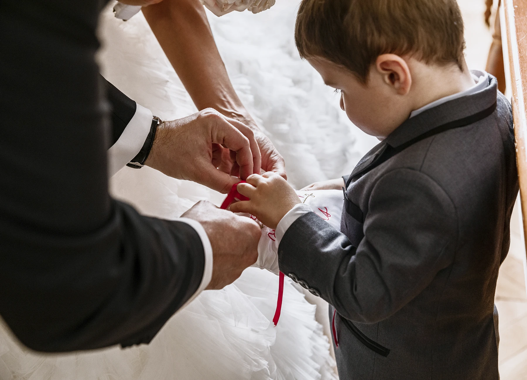 Mariés penchés vers un petit garçon présentant les alliances. Photo par Laurène Zabary