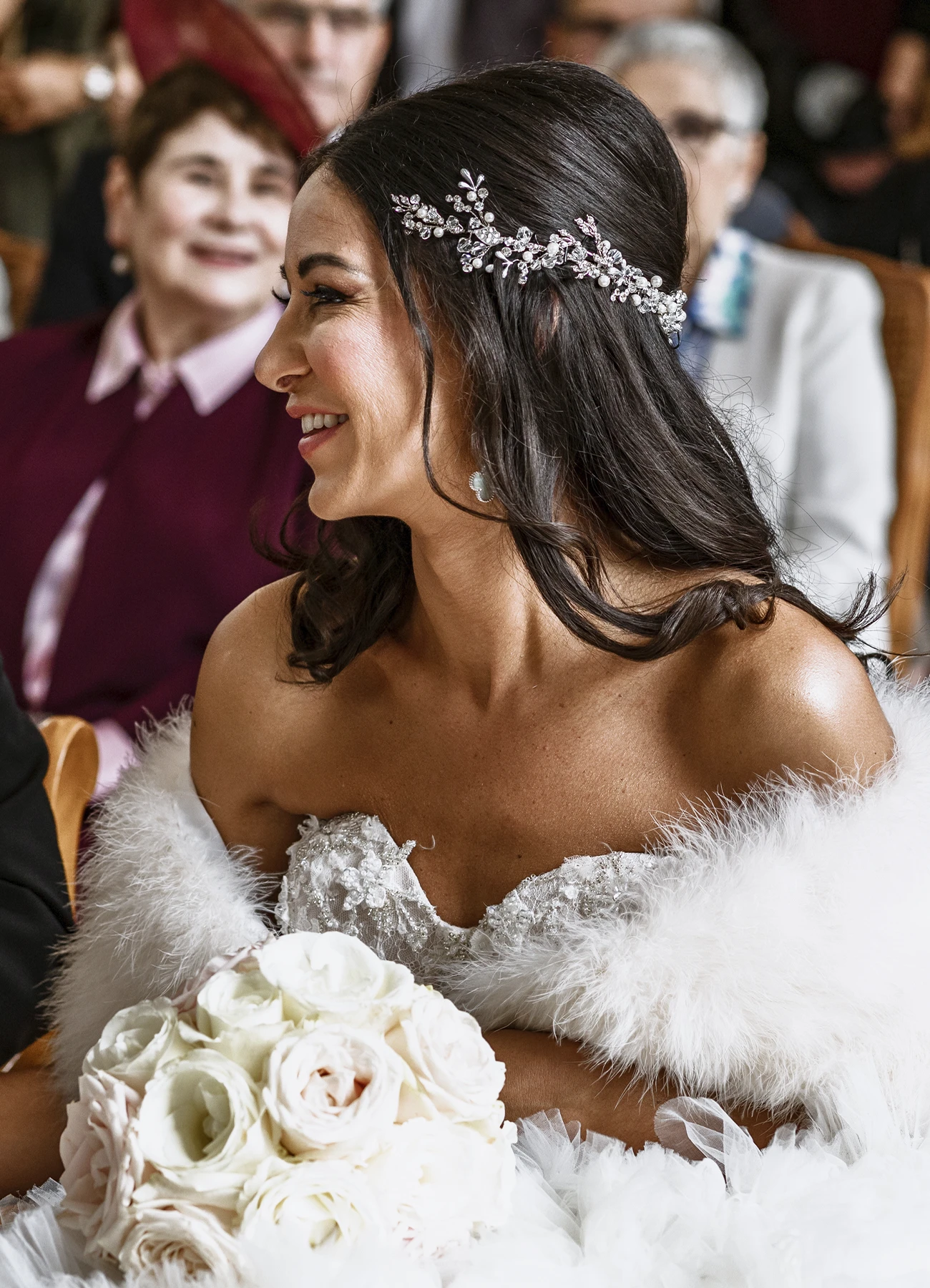 Portrait souriant de la mariée tenant son bouquet, assise, tournant la tête vers la gauche. Photo par Laurène Zabary