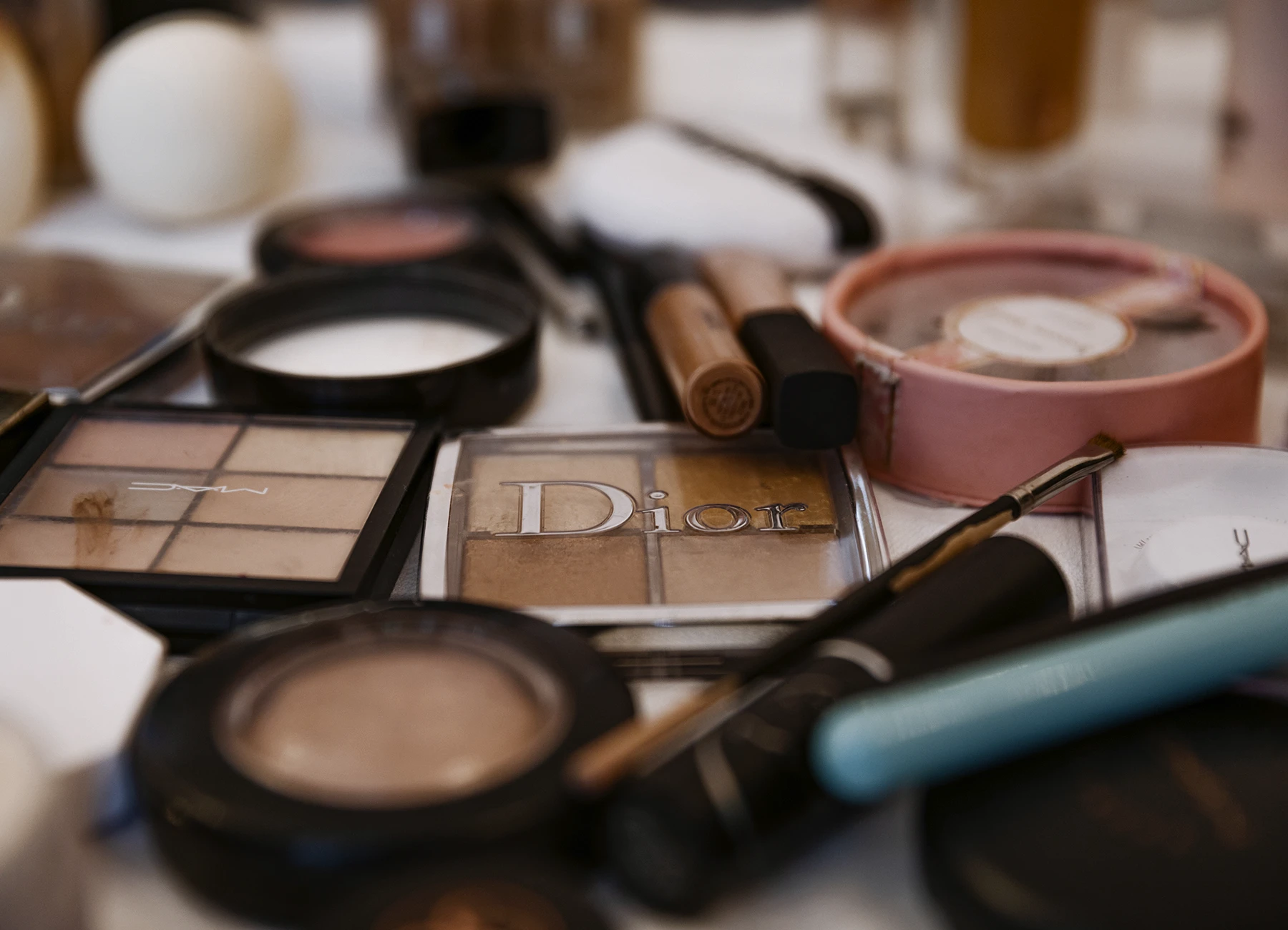 Poudrier Dior entouré de palettes de maquillage et pinceaux. Photo par Laurène Zabary