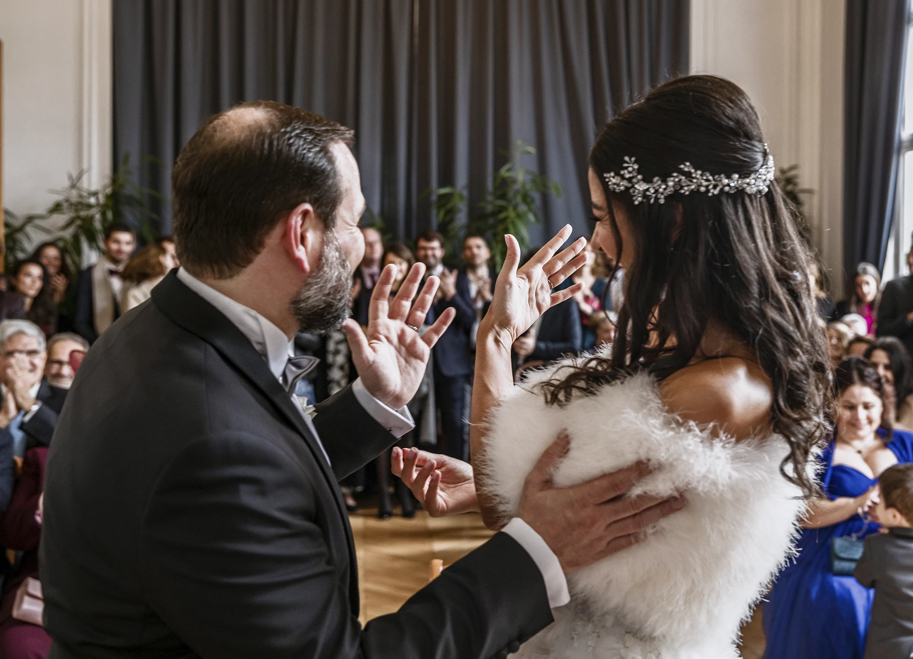 Mariés tournant le dos à l'objectif, montrant leurs alliances à l'assistance applaudir dans la mairie. Photo par Laurène Zabary