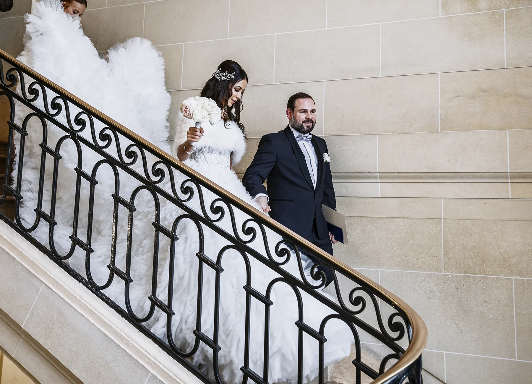 Les mariés descendant les escaliers de la mairie, la traîne de la mariée est portée derrière elle. Photo par Laurène Zabary