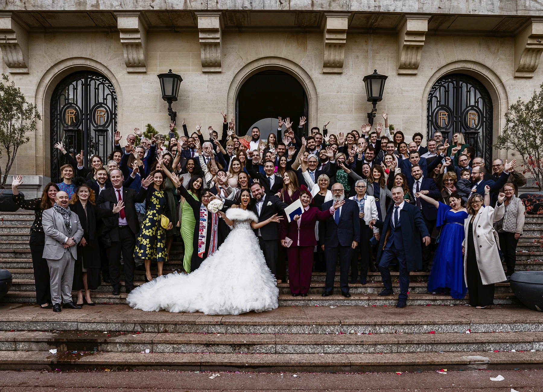 Photo de groupe dynamique sur les marches de la mairie d'Aulnay-sous-Bois, les mariés au centre entourés de joyeux invités. Photo par Laurène Zabary