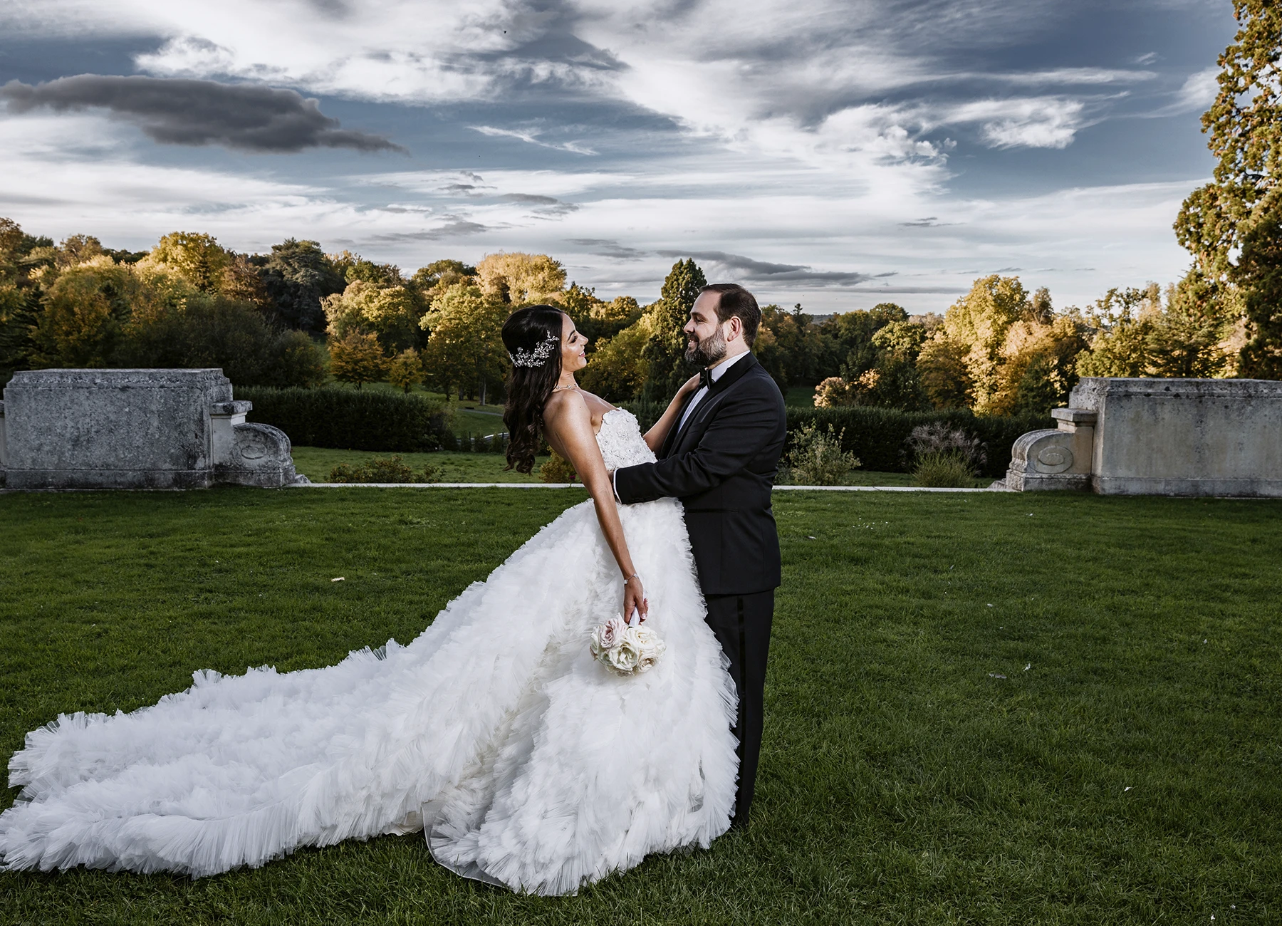 Couple posant devant le vaste parc verdoyant du Château Bouffémont sous un ciel bleu parsemé de nuages. Photo par Laurène Zabary