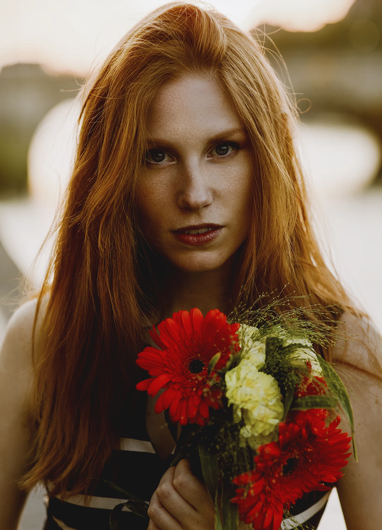 Portrait de Fiona, jeune femme rousse avec taches de rousseur, tenant un bouquet de fleurs en extérieur à Paris, en fin de journée. Photo par Laurène Zabary