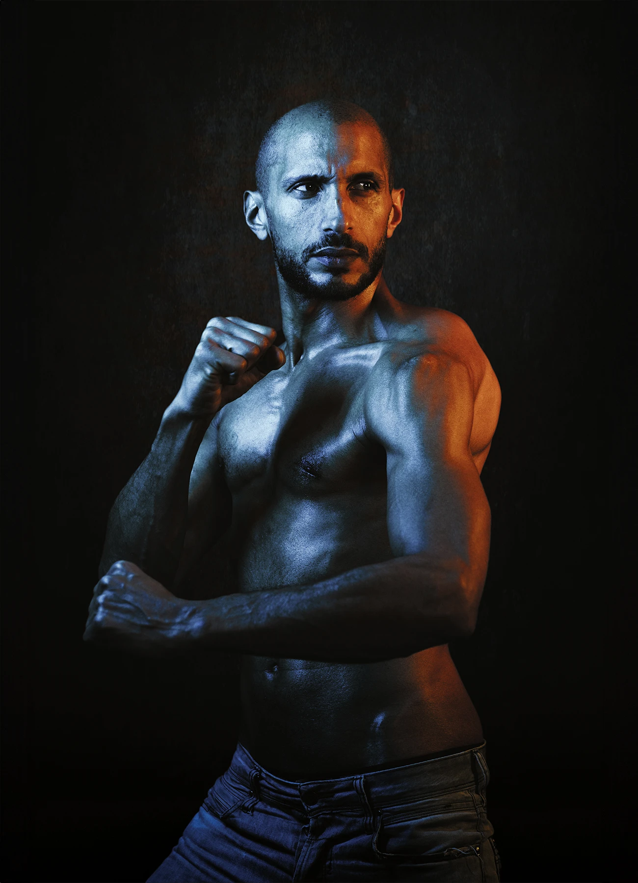 Portrait de Mike en posture défensive, éclairé par des lumières jaunes et bleues sur fond noir.