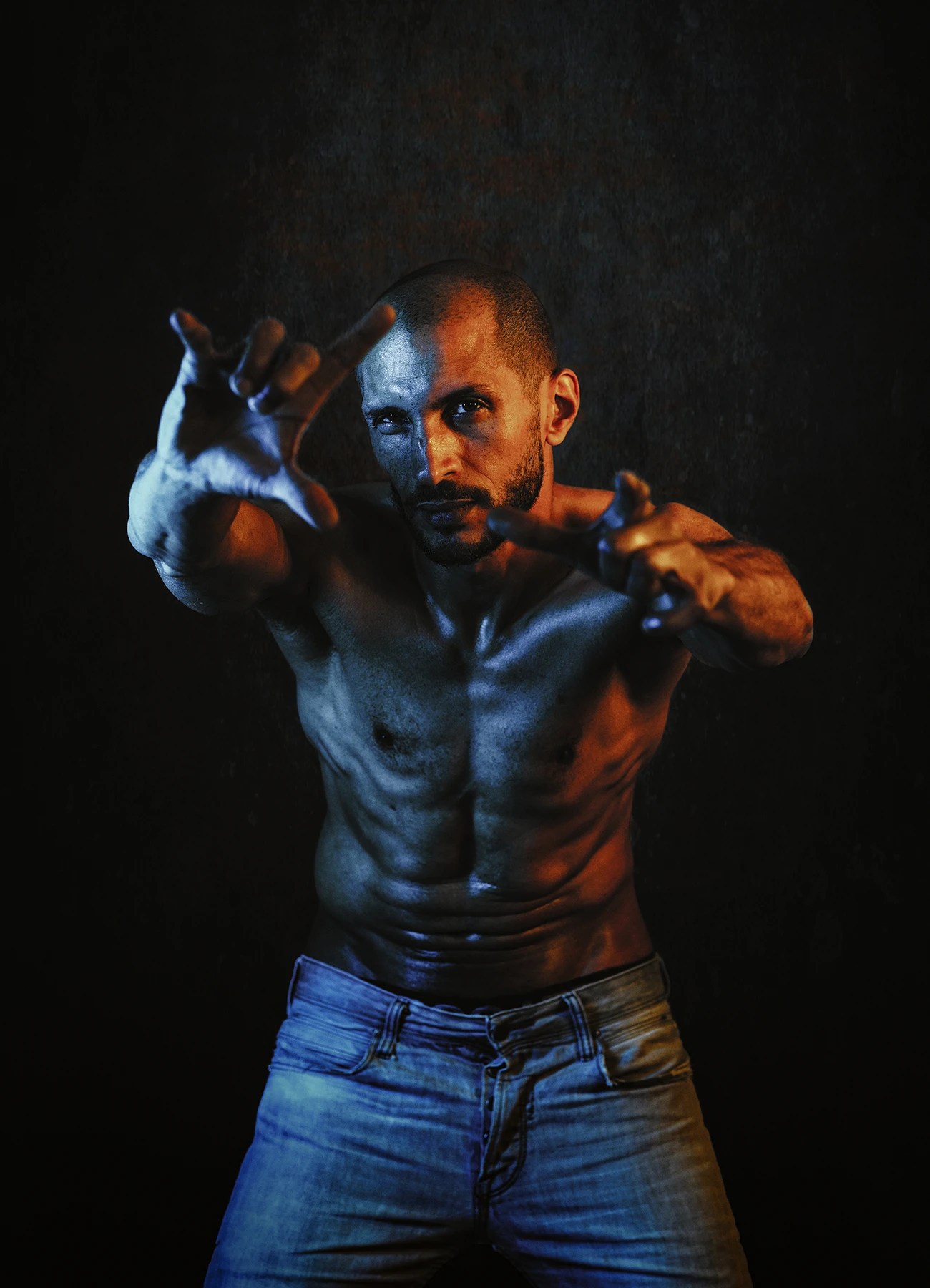 Portrait de Mike, comédien torse nu, regard détendu vers l'objectif, éclairé par des lumières jaunes et bleues sur fond noir.