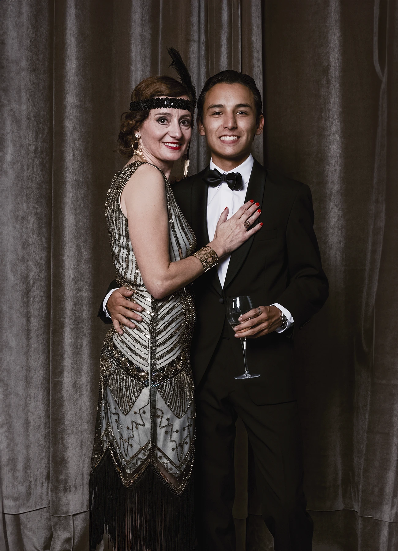 Portrait d’une femme et d’un homme tenant un verre de champagne, posant devant une draperie, réalisé lors d’une soirée d’anniversaire sur le thème des années 20 à l’hôtel Vernet par Laurène Zabary.