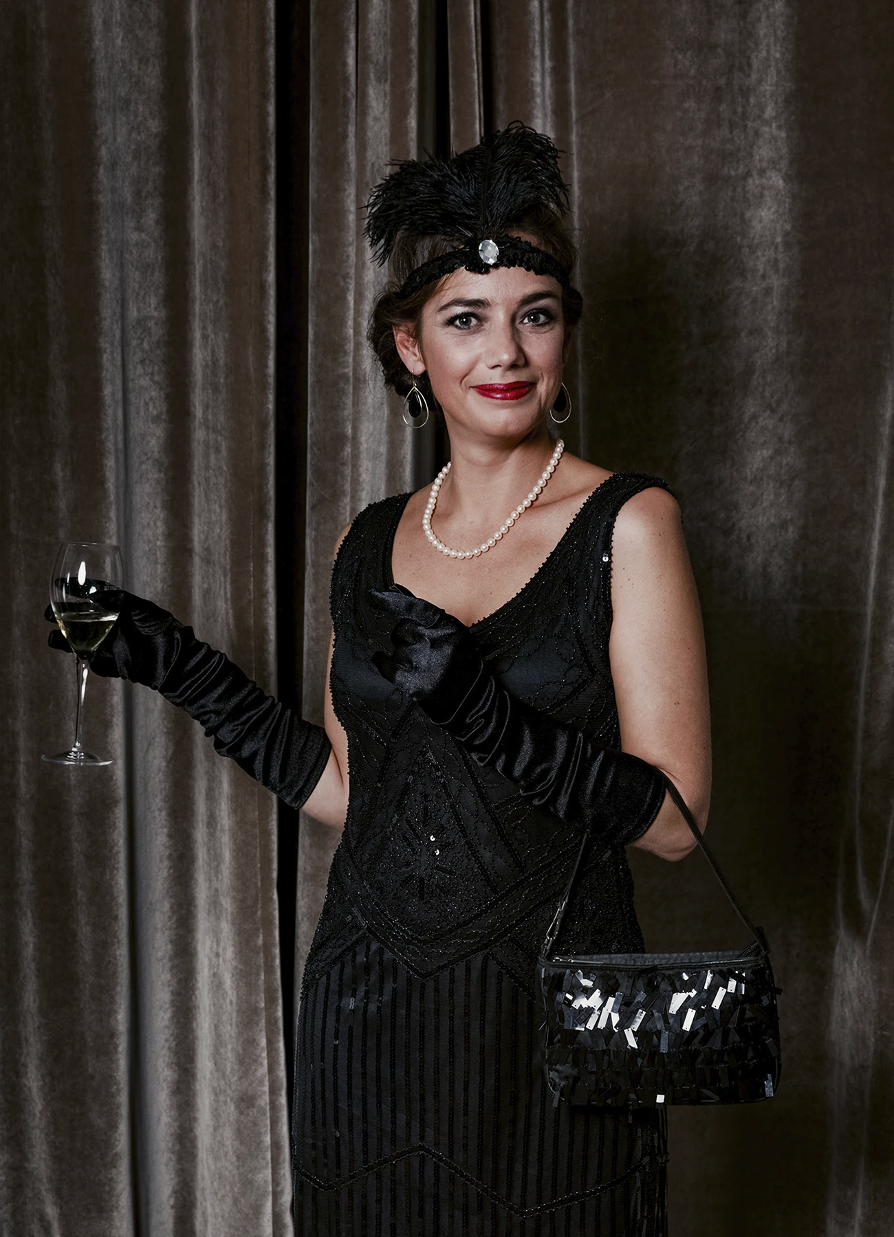 Portrait d’une femme tenant un verre de champagne et un sac à main devant une draperie, réalisé lors d’une soirée d’anniversaire à l’hôtel Vernet par Laurène Zabary.