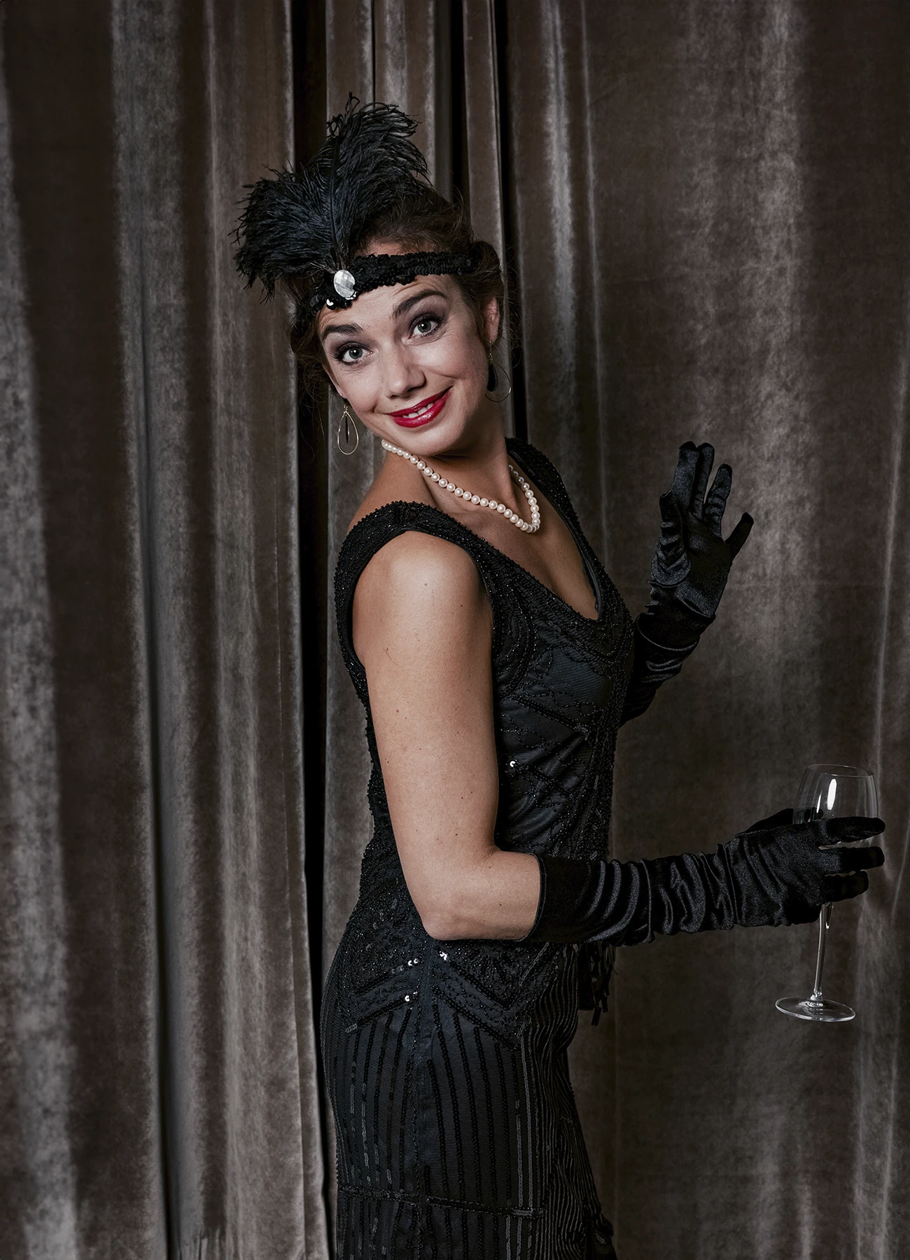 Portrait d’une femme tenant un verre de champagne devant une draperie, réalisé lors d’une soirée d’anniversaire sur le thème des années 20 à l’hôtel Vernet par Laurène Zabary.