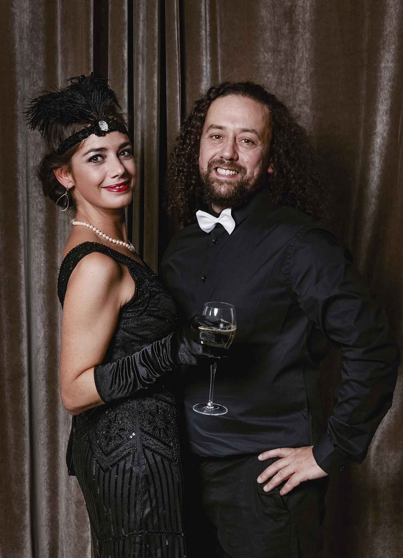 Portrait d’un homme et d’une femme tenant un verre de champagne, posant devant une draperie, réalisé lors d’une soirée d’anniversaire sur le thème des années 20 à l’hôtel Vernet par Laurène Zabary.