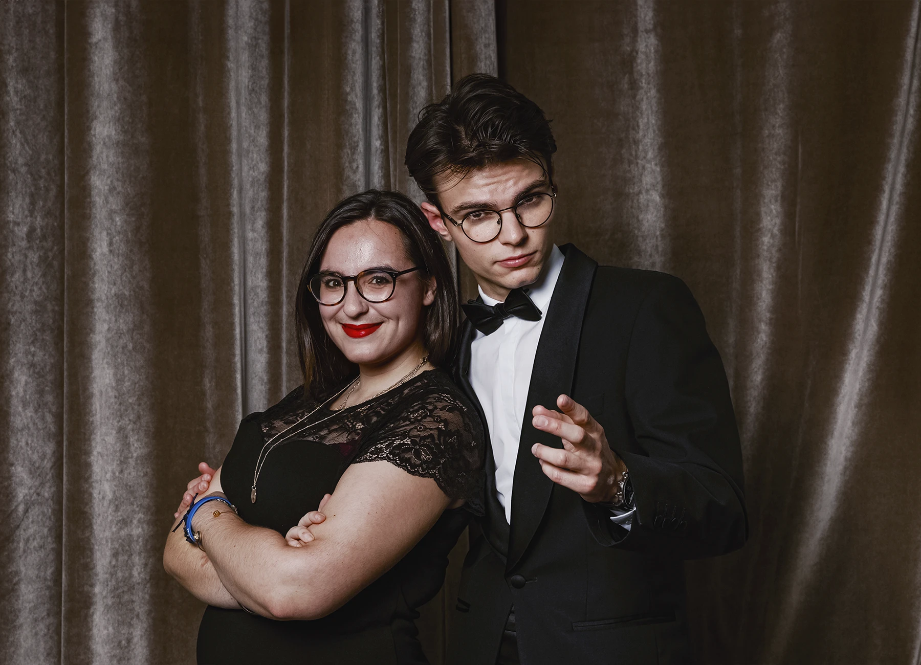 Portrait d’un homme et d’une femme, l’homme faisant un signe vers l’appareil, pris devant une draperie, réalisé lors d’une soirée d’anniversaire sur le thème des années 20 à l’hôtel Vernet par Laurène Zabary.