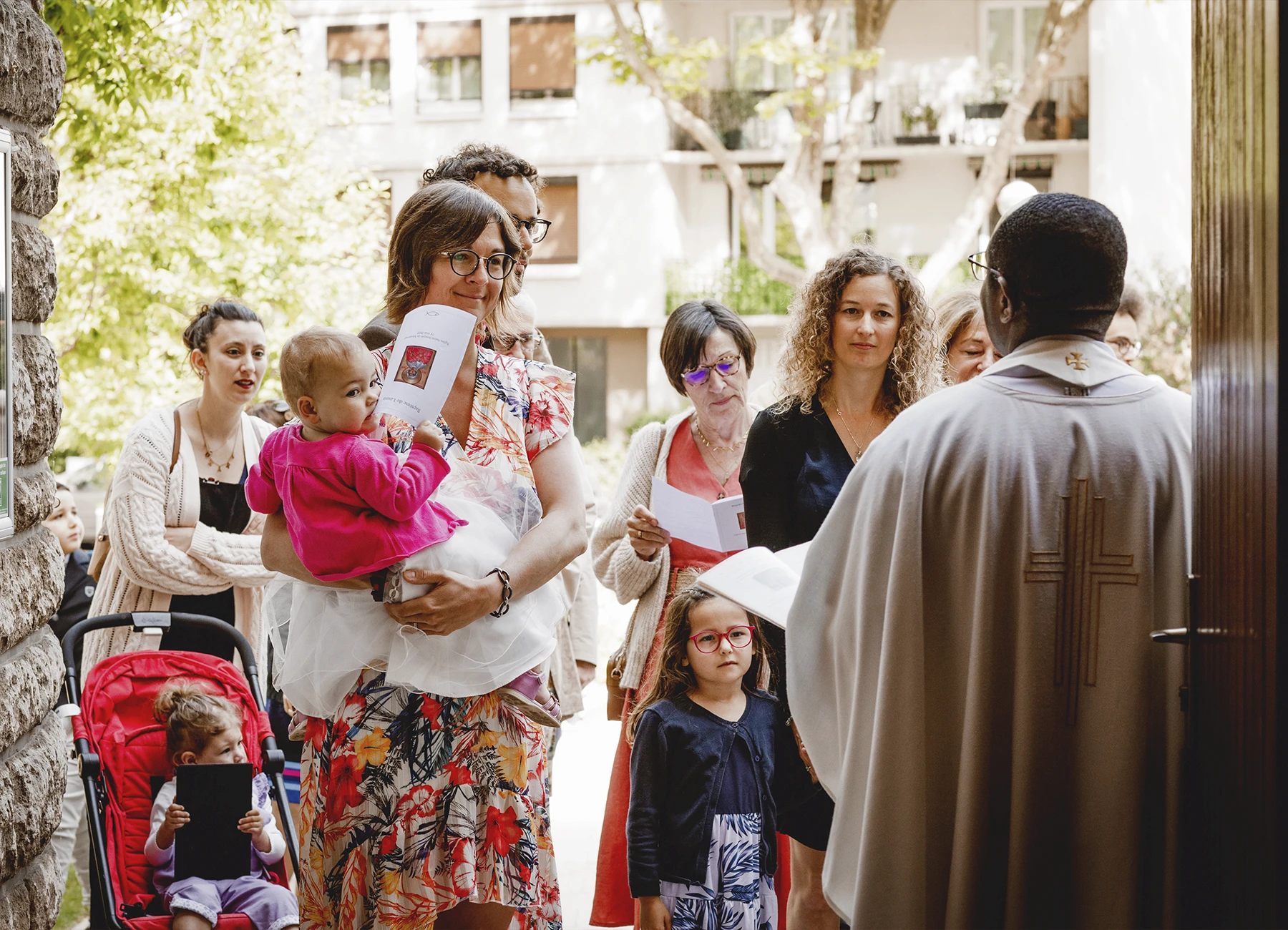 La famille réunie écoute le prêtre à l’extérieur de l’église Saint-Joseph de Montrouge avant d’y entrer pour la cérémonie de baptême, capturée par Laurène Zabary.