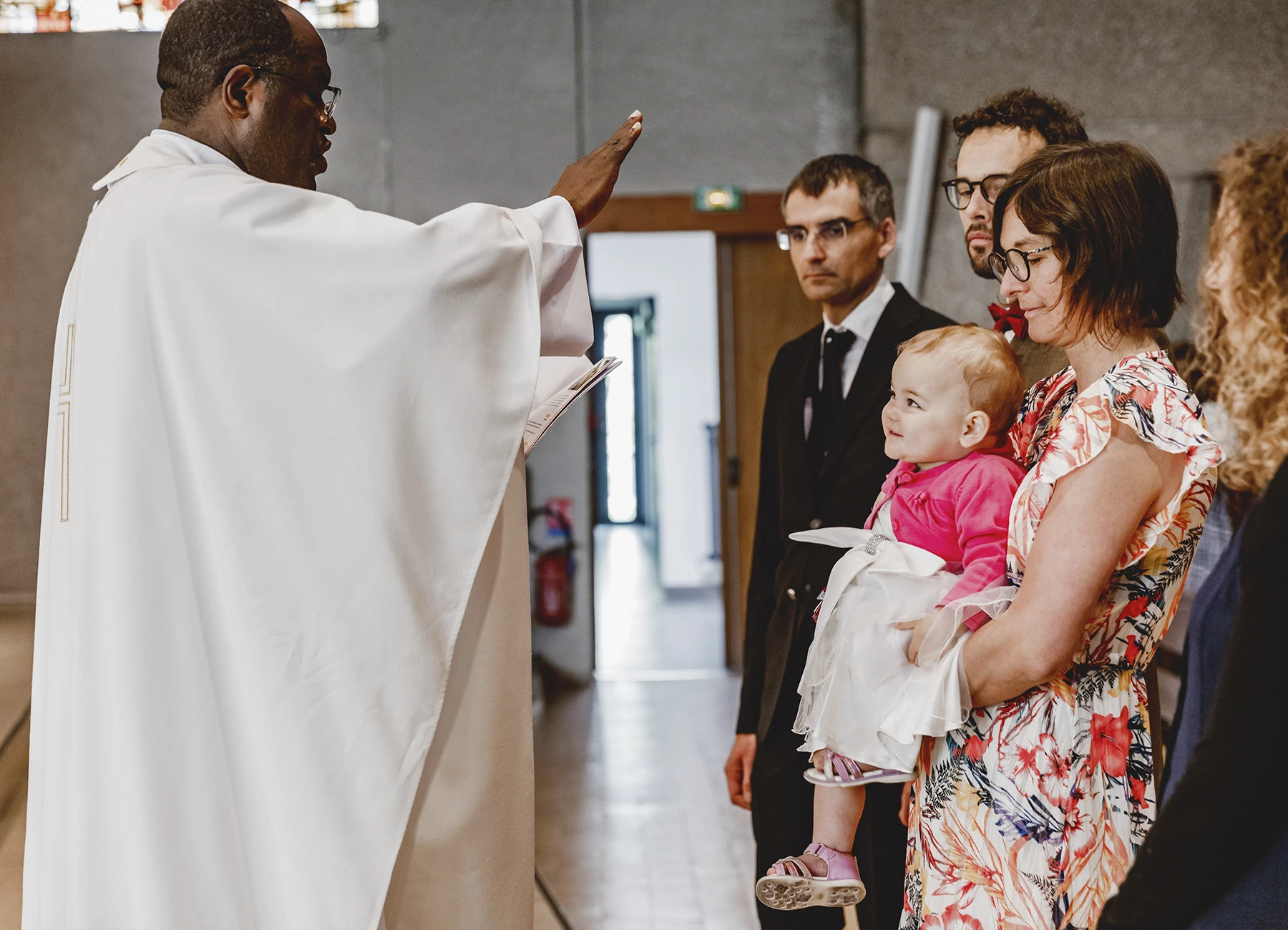 Le prêtre bénit le couple et leur enfant après le baptême à l’église Saint-Joseph de Montrouge, capturé par Laurène Zabary.