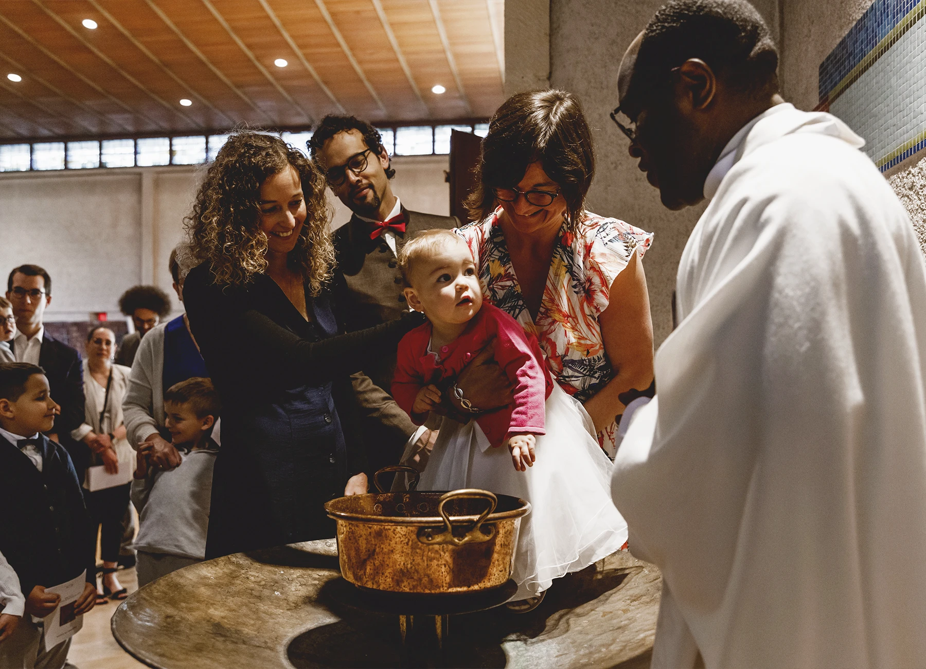 Le bébé, tenu par sa mère, regarde le prêtre après avoir été baptisé à l’église Saint-Joseph de Montrouge, immortalisé par Laurène Zabary.