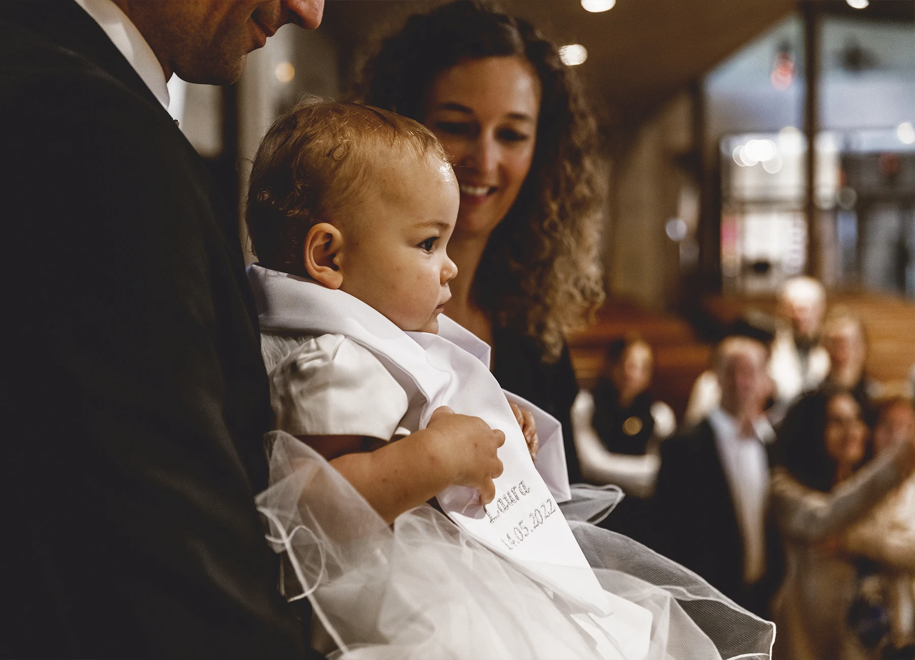 Gros plan sur le bébé tenu par son parrain durant la cérémonie de baptême à l’église Saint-Joseph de Montrouge, photographié par Laurène Zabary.
