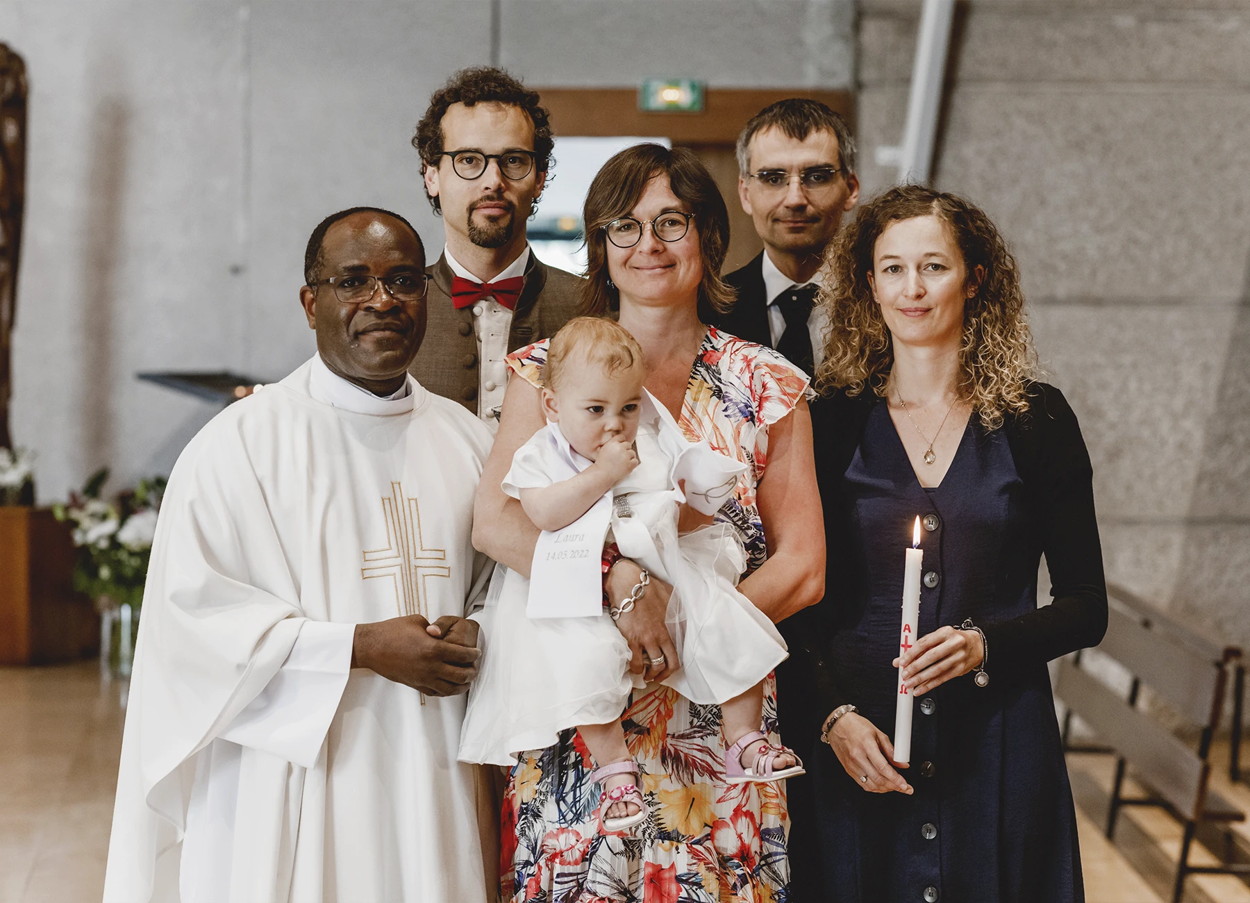 Le couple, le bébé, le parrain, la marraine et le prêtre posent ensemble dans l’église Saint-Joseph de Montrouge après un baptême, photographiés par Laurène Zabary.