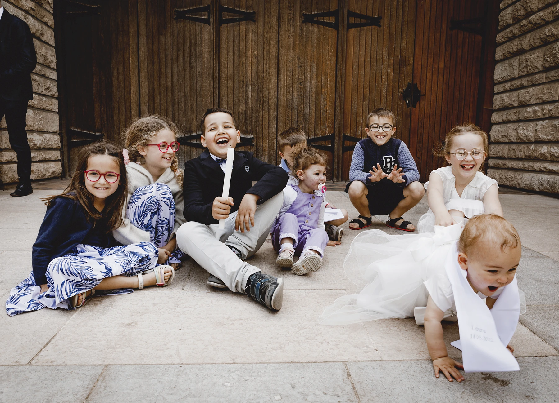 Le bébé s’échappe à quatre pattes tandis que les enfants rient, capturé lors d’un baptême à l’église Saint-Joseph de Montrouge par Laurène Zabary.