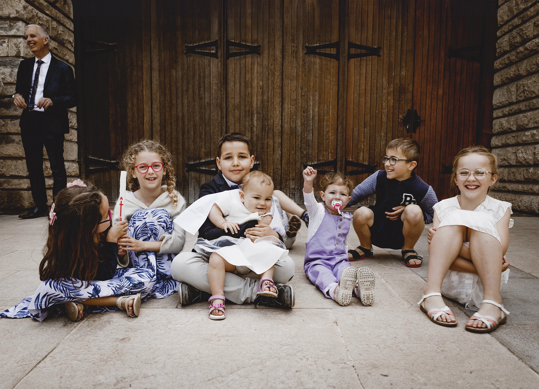 Les enfants de la famille, assis devant le parvis de l’église avec le bébé, photographiés lors d’un baptême à Saint-Joseph de Montrouge par Laurène Zabary.