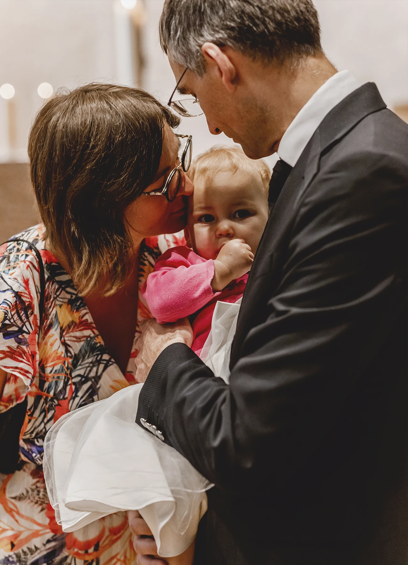 Une mère embrasse tendrement son enfant tenu par son parrain lors d’un baptême à l’église Saint-Joseph de Montrouge, capturé par Laurène Zabary.