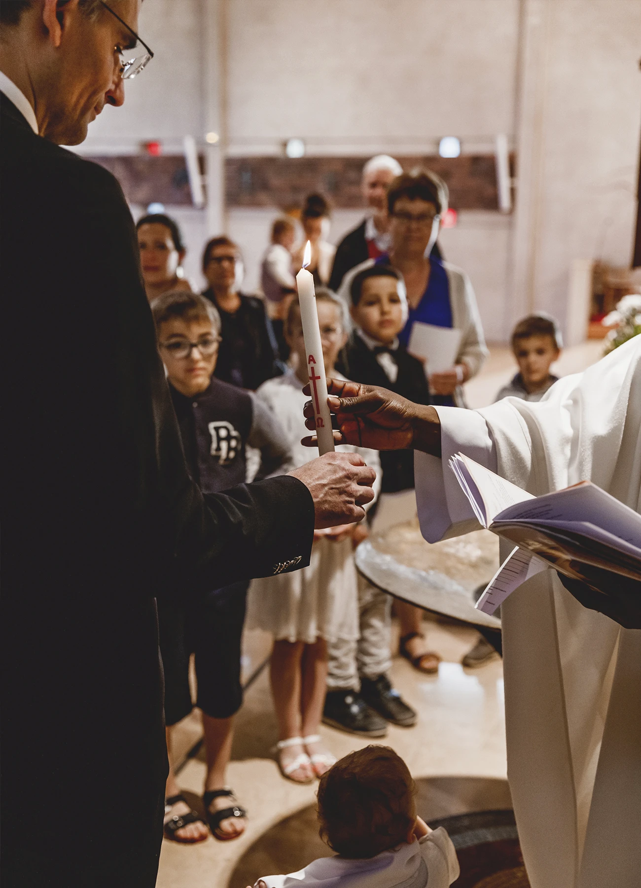 Le prêtre et le témoin tenant un cierge lors d’un baptême à l’église Saint-Joseph de Montrouge, immortalisé par Laurène Zabary.
