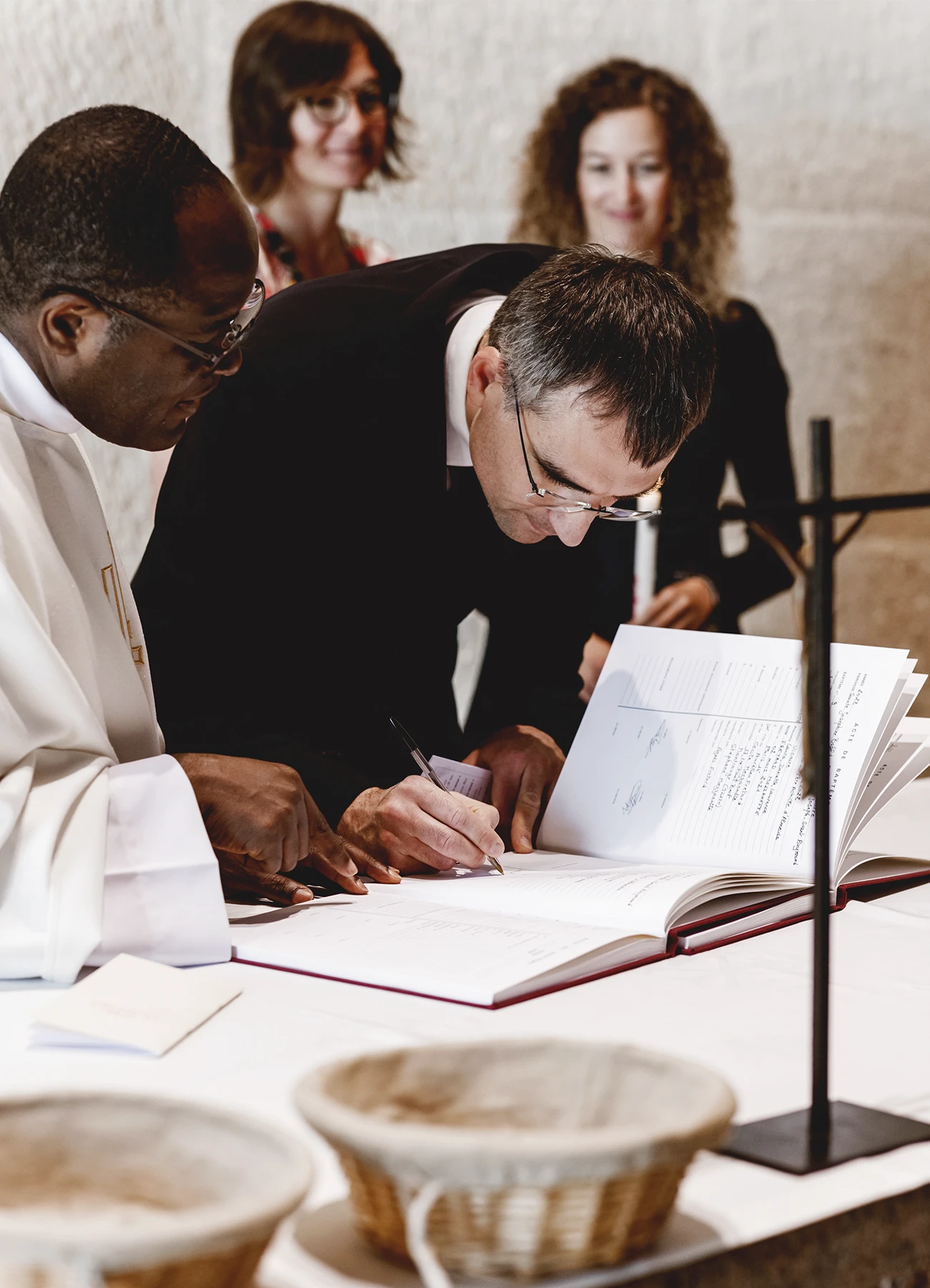 Un témoin signe le registre sous le regard du prêtre lors d’un baptême à l’église Saint-Joseph de Montrouge, capturé par Laurène Zabary.