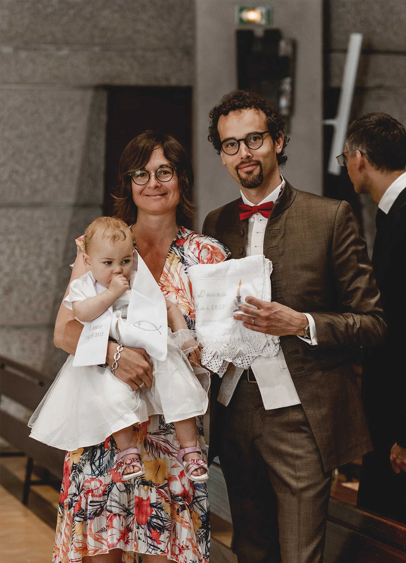Le couple et le bébé à baptiser se tiennent debout dans l'église Saint-Joseph de Montrouge avant le début de la cérémonie, capturé par Laurène Zabary, photographe à Paris.