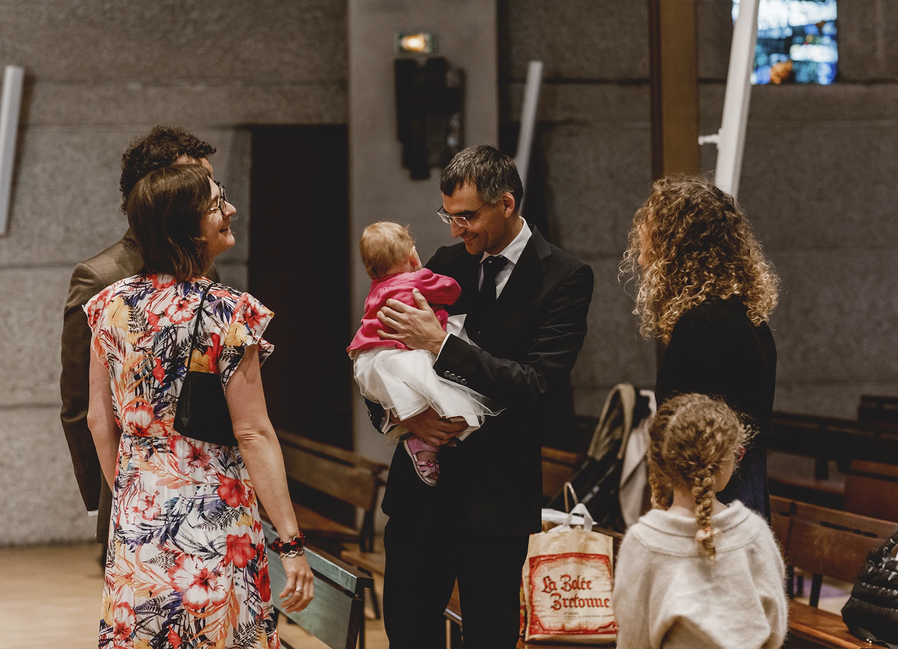 La famille est réunie autour du bébé dans l’église Saint-Joseph de Montrouge pendant la cérémonie de baptême, capturée par Laurène Zabary.