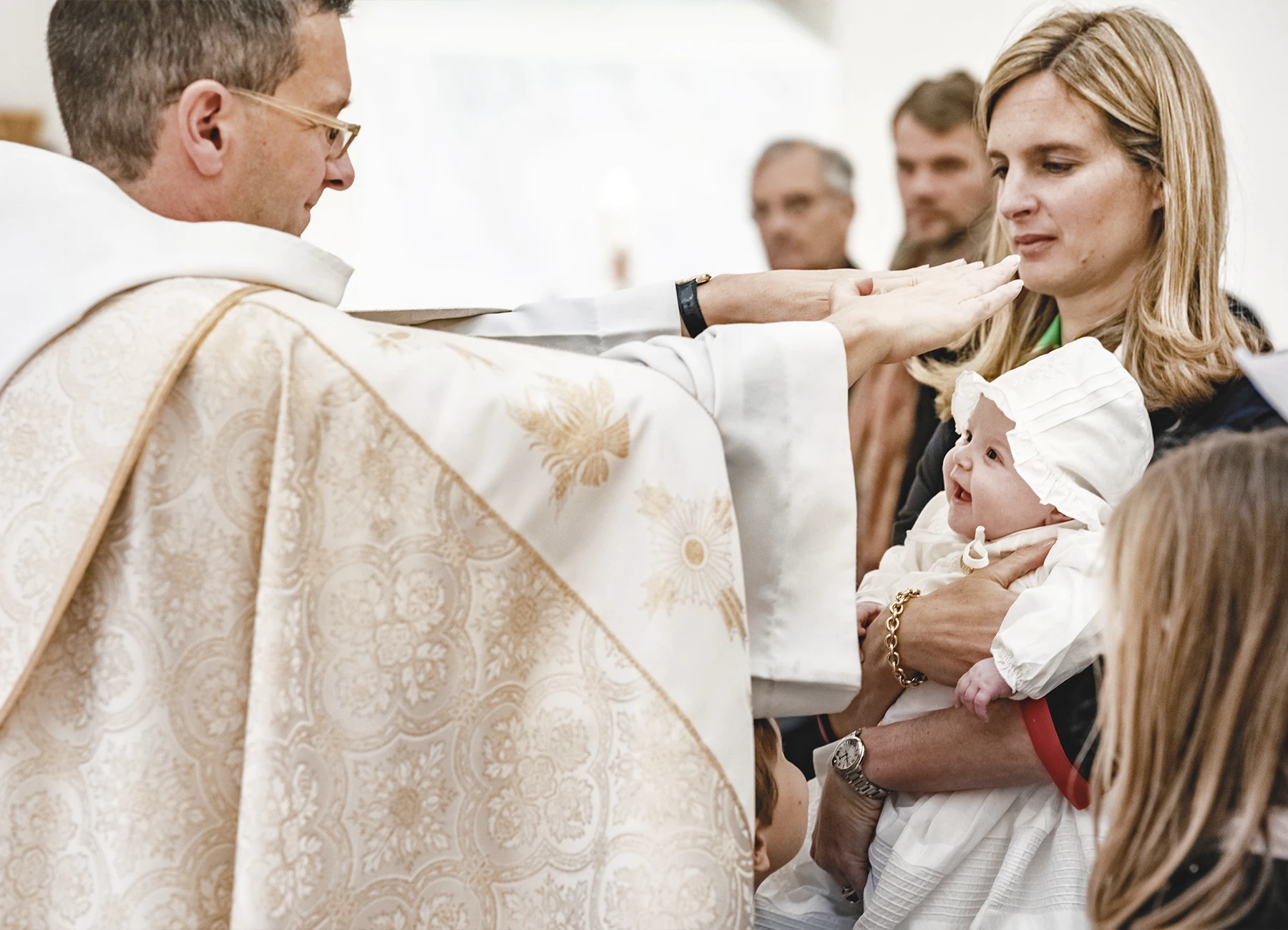 Le prêtre bénissant le deuxième bébé, souriant dans les bras de sa mère.