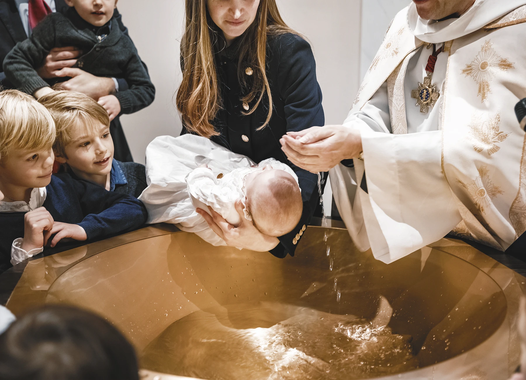 Le prêtre applique de l’eau sur la tête du premier bébé pour le baptiser.
