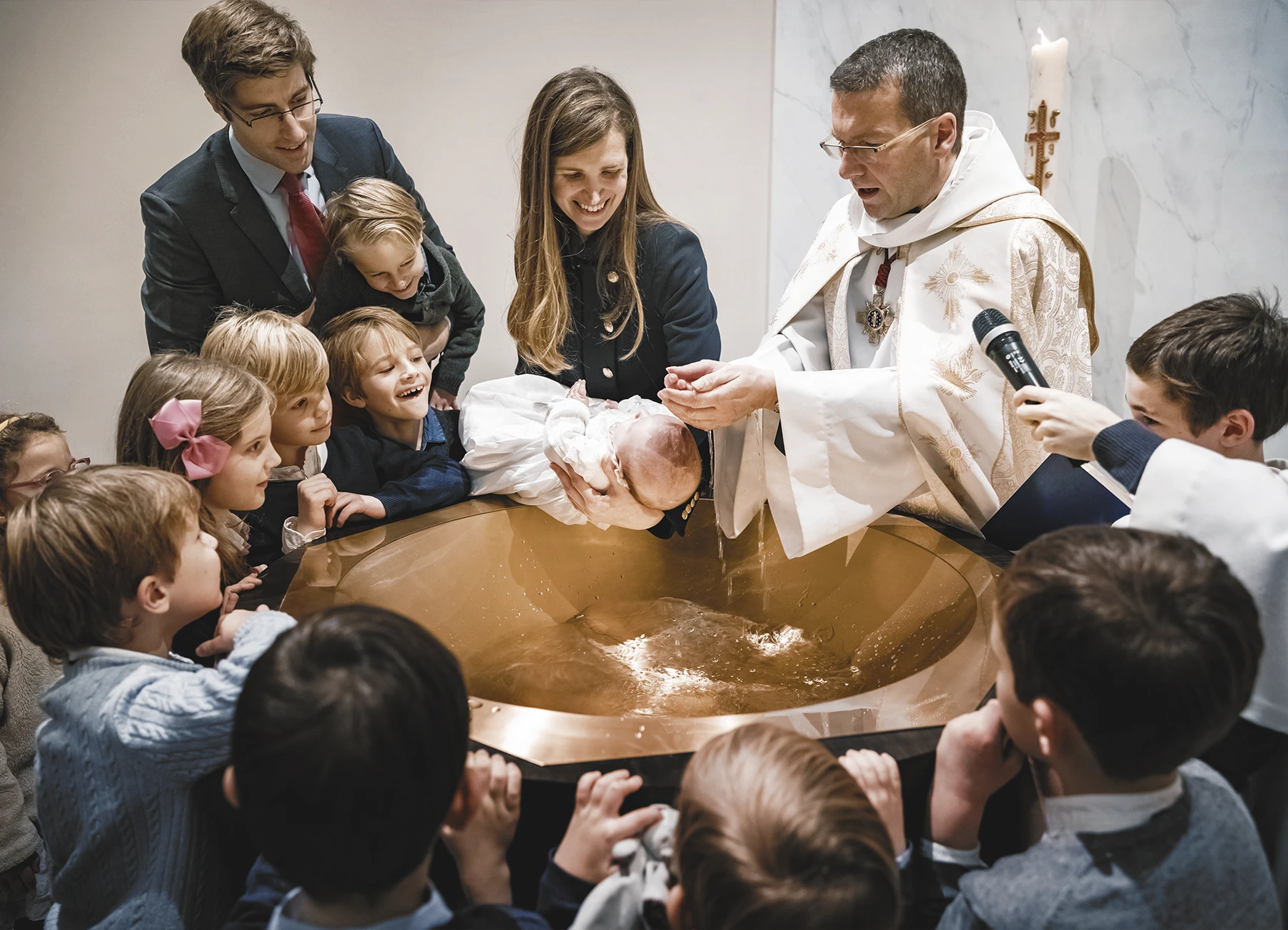 Le prêtre applique de l’eau sur la tête du premier bébé pour le baptiser.